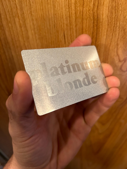 Hand holding a metallic Silver gift card with 'Platinum Card' text laser engraed, presented against a wooden background
