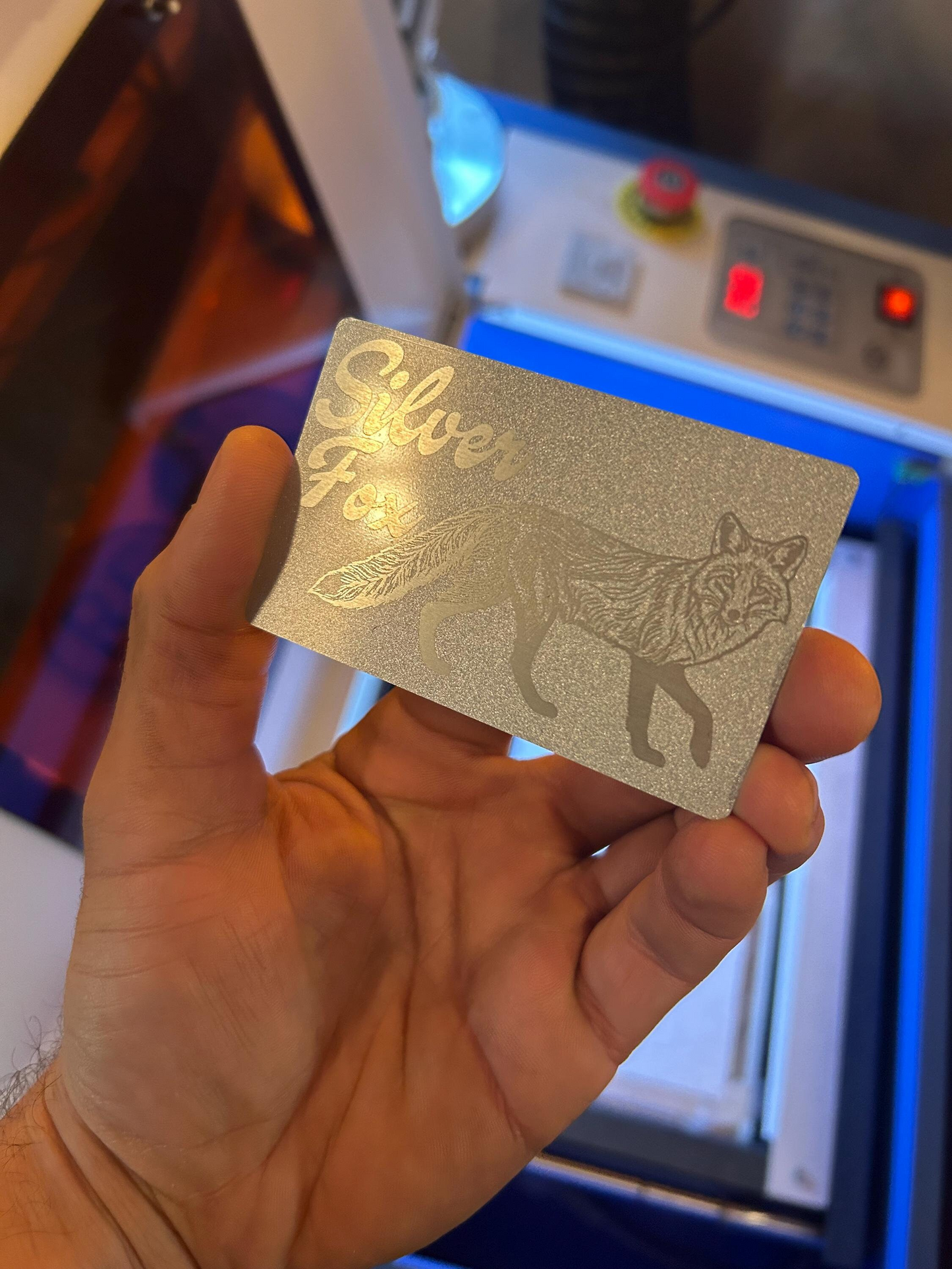Hand holding a silver and silver card with 'Silver Fox' and a Fox design in front of a machine.