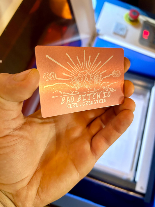 Hand holding a small metal card with engraved text and design.