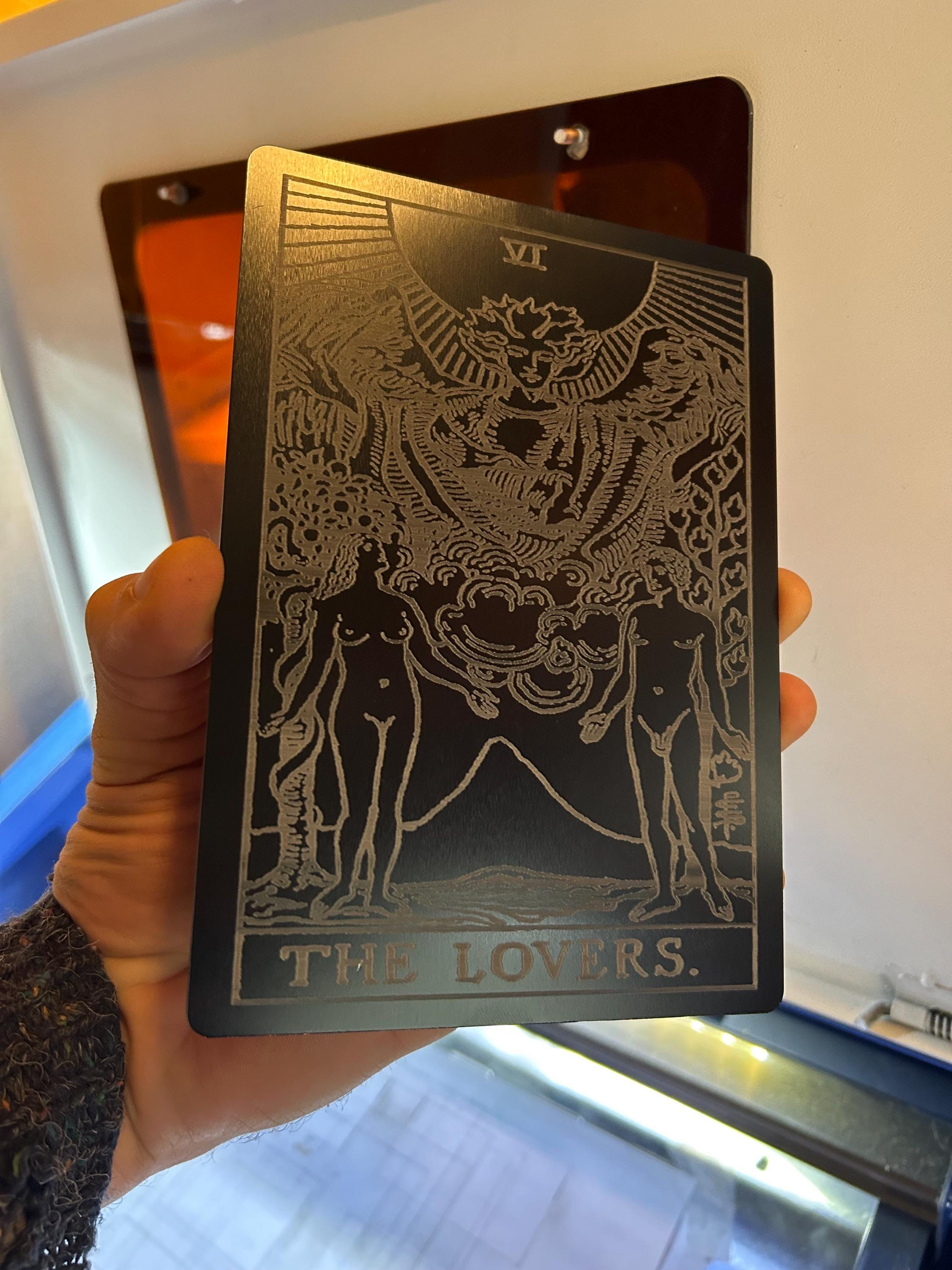 Hand holding a 5x7 large metal plaque, with The Lovers tarot card laser engraved in silver