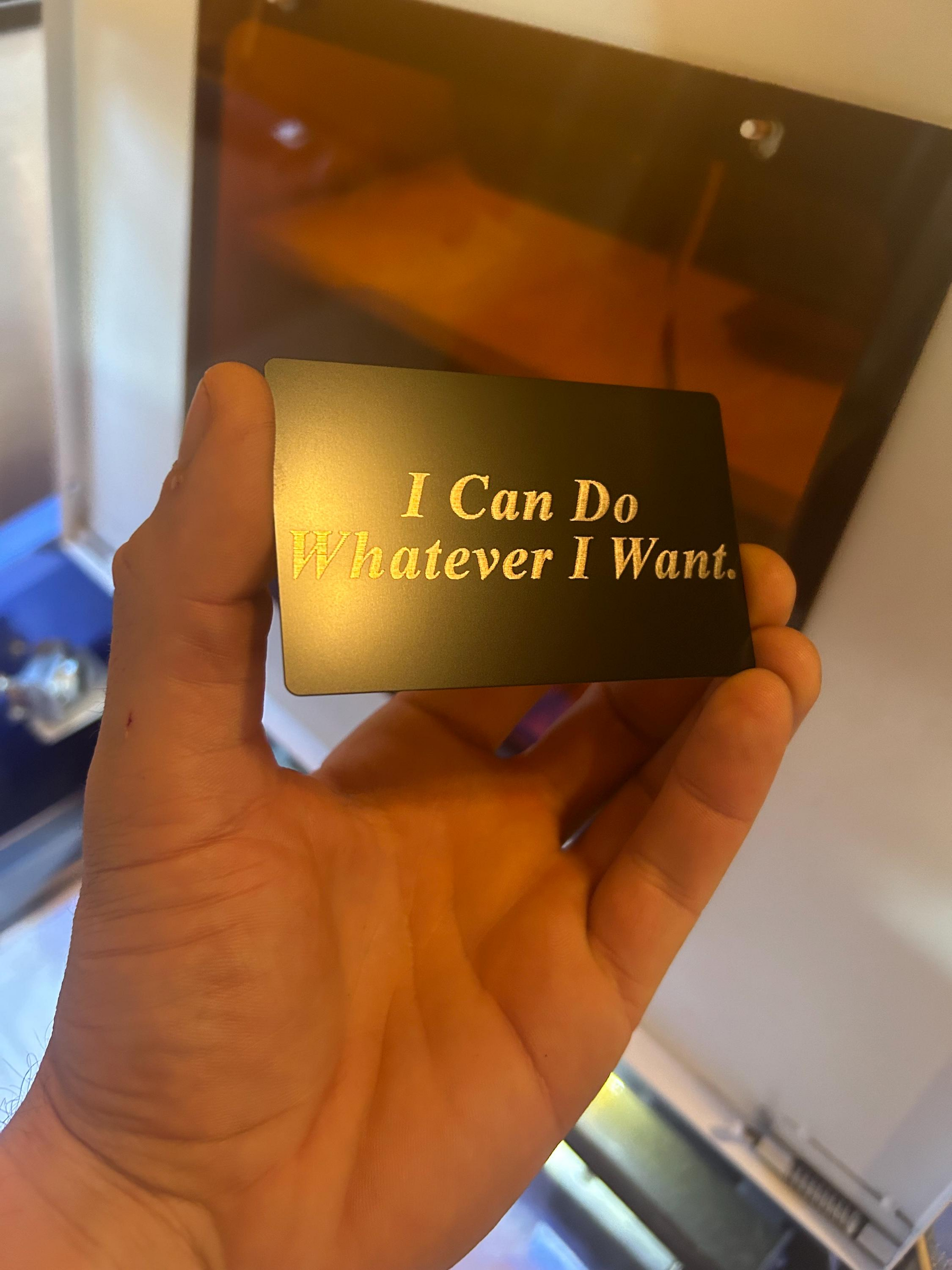 Hand holding a black metal card with funny 'I Can Do Whatever I Want' text engraved