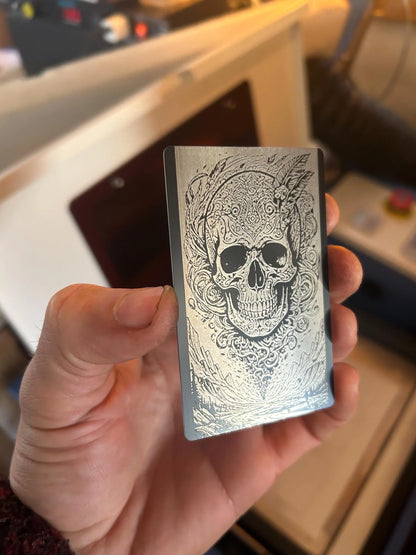 Hand holding a metallic card with an intricate human skull design against a blurred industrial background