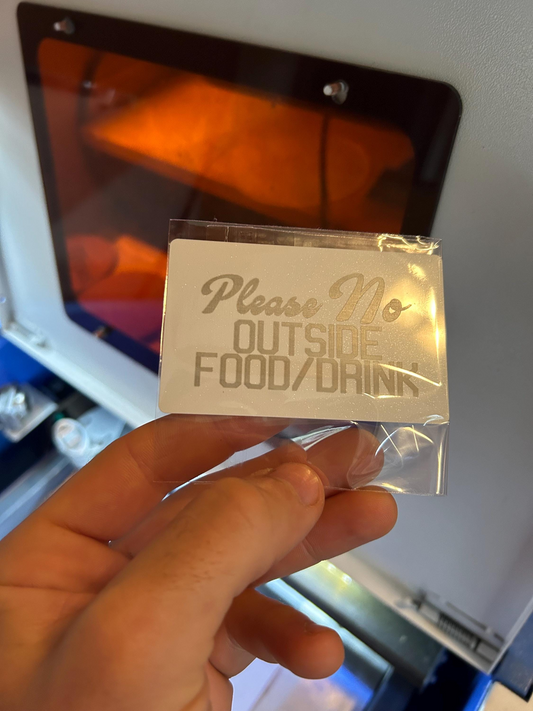 Hand holding a white and silver metal business card, in cellophane shipping pack for customized text engraving