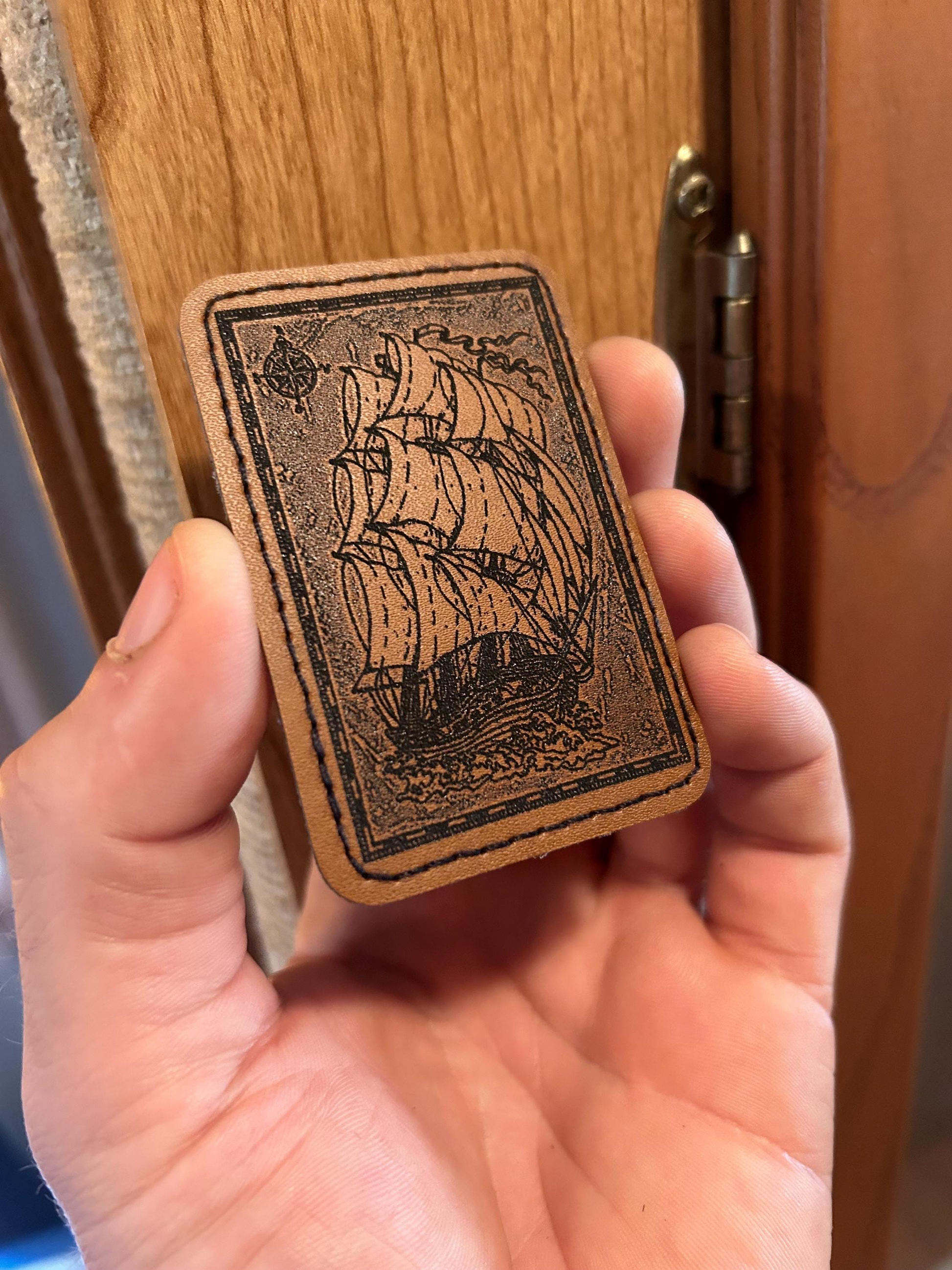 Hand holding a small leather-patch with a ship illustration on a wooden door background
