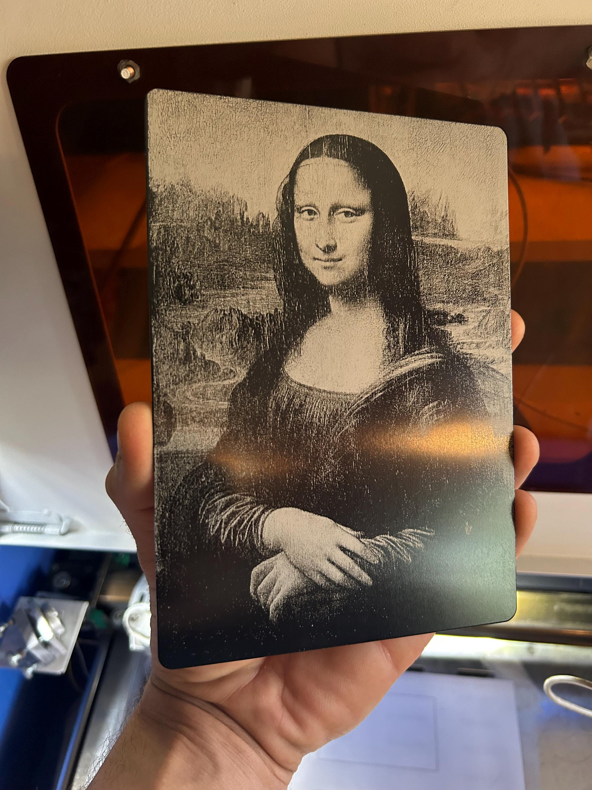 Hand holding a 5x7 anodized aluminum decorative plaque with highly detailed laser engraving of The Mona Lisa 