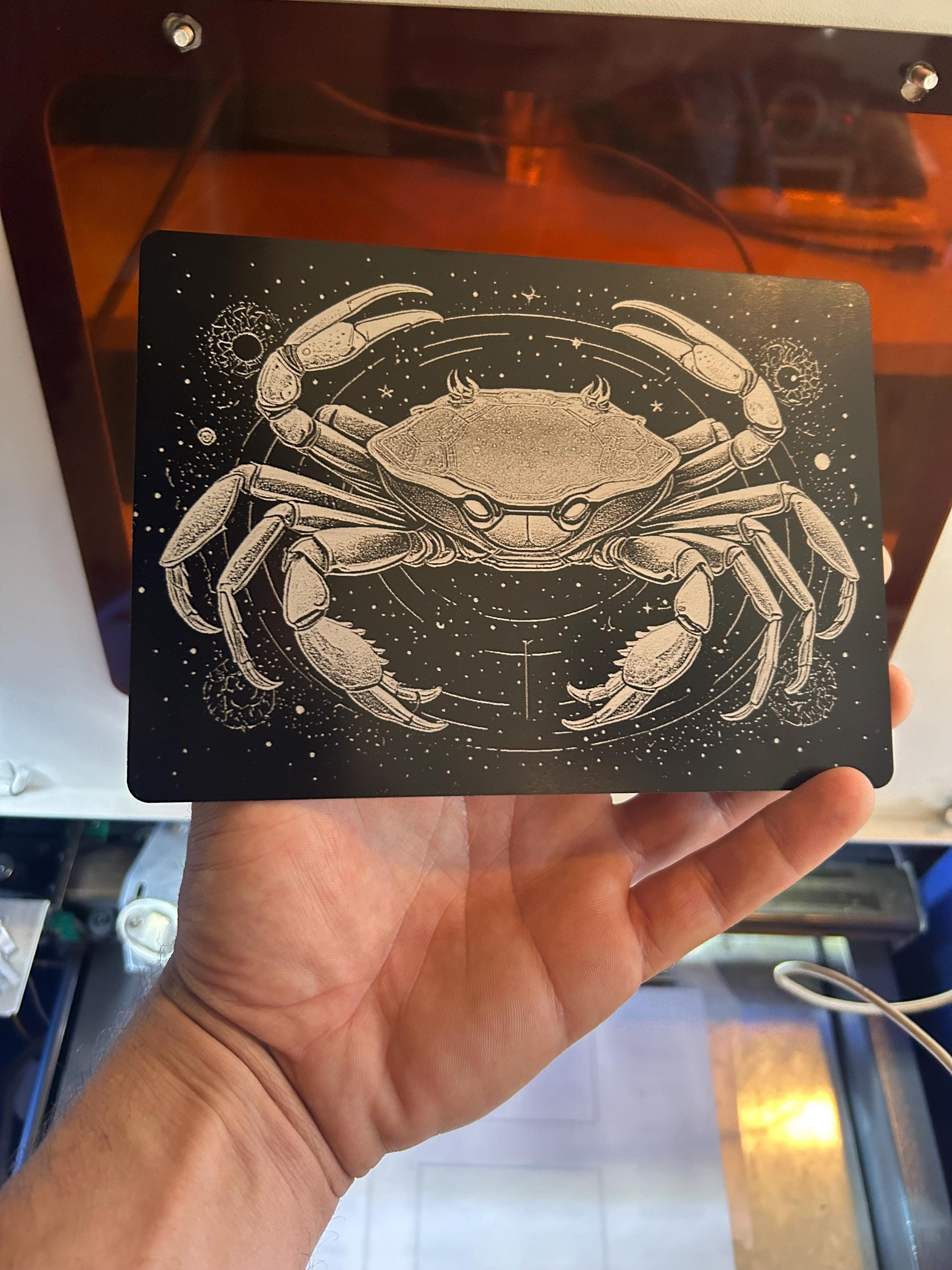 Hand holding a laser engraved 5x7 inch metal placard with a crab design against a starry background