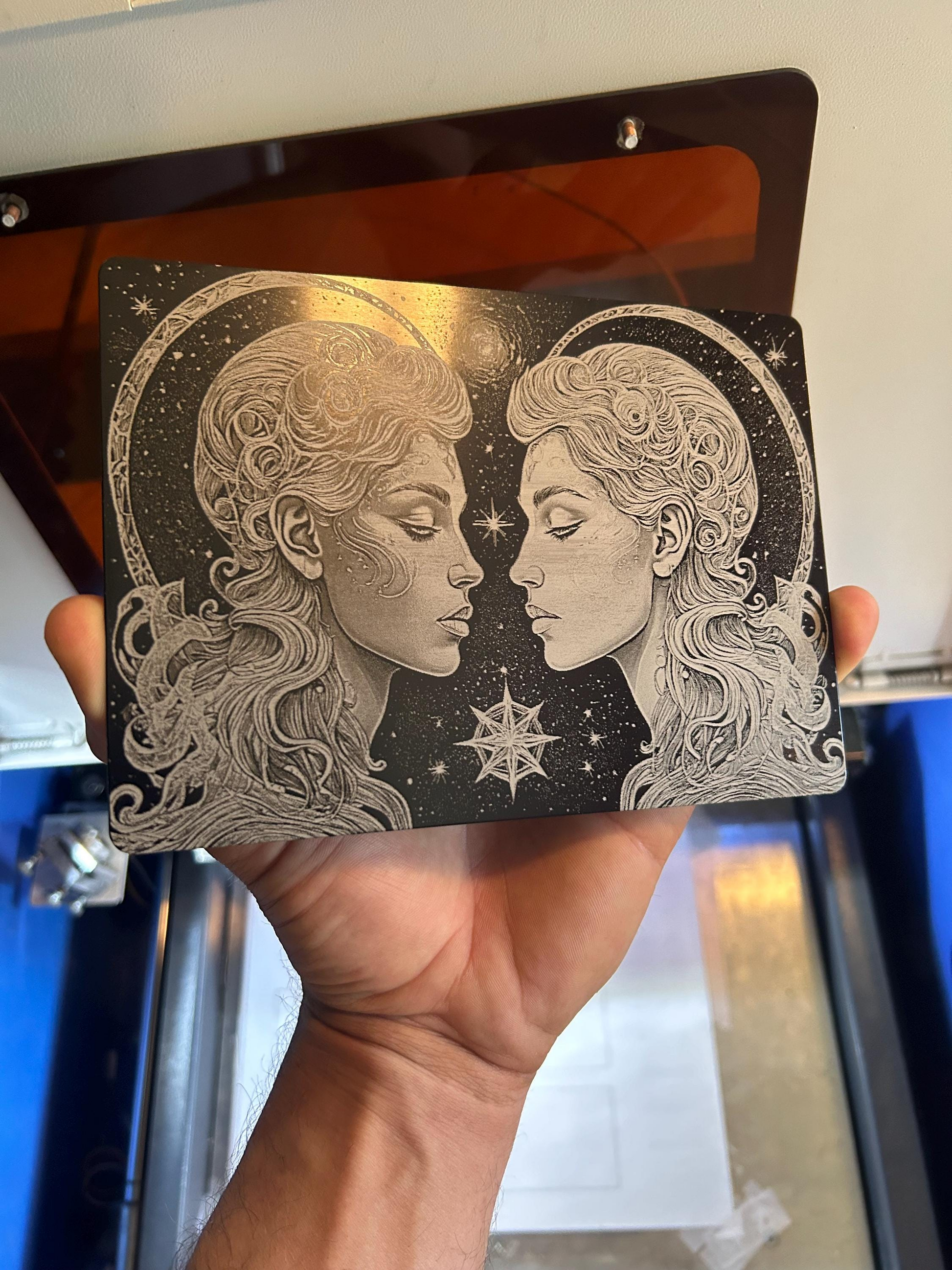 Hand holding a decorative plaque with two faces as the Gemini Twins and spiritual astrological star designs.