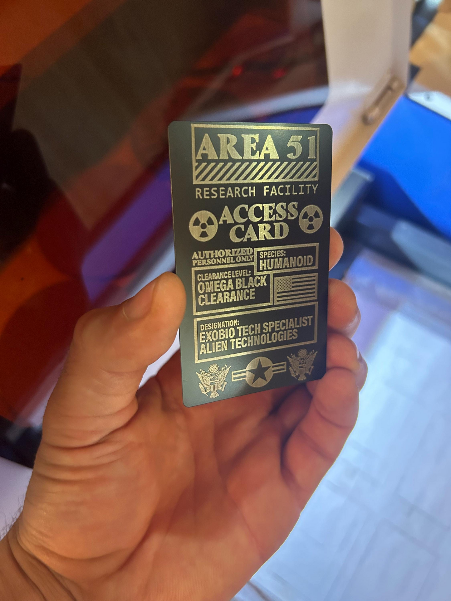 Hand holding black silver area 51 access card, with laser engraved text details
