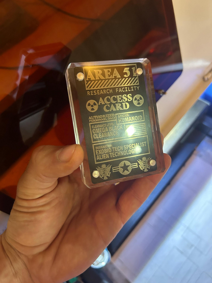 Hand holding a themed 'Area 51' access card against a blurred background, shown in an acrylic display case