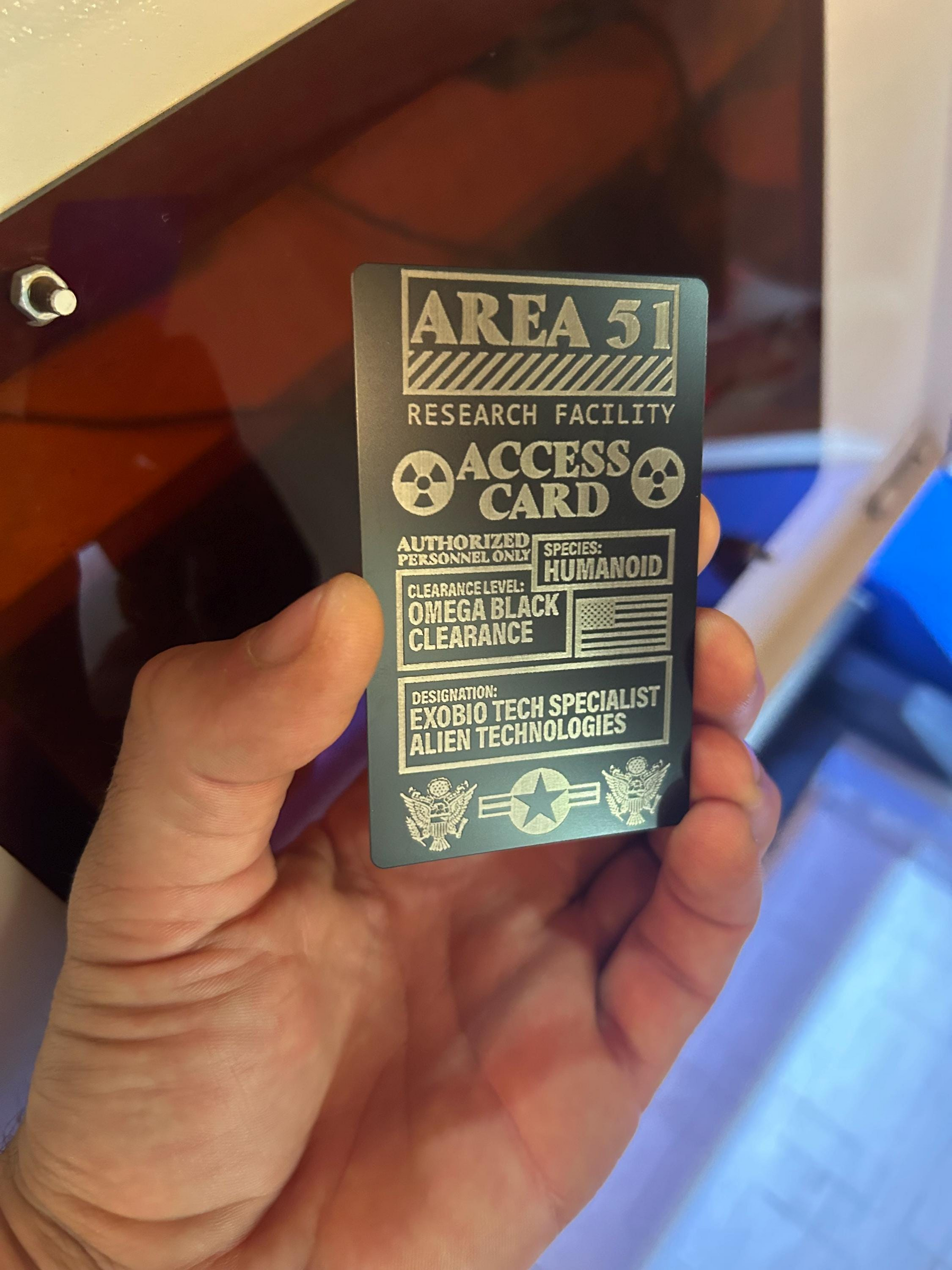 Hand holding an anodized aluminum laser engraved novelty Area 51 research facility access gift wallet card