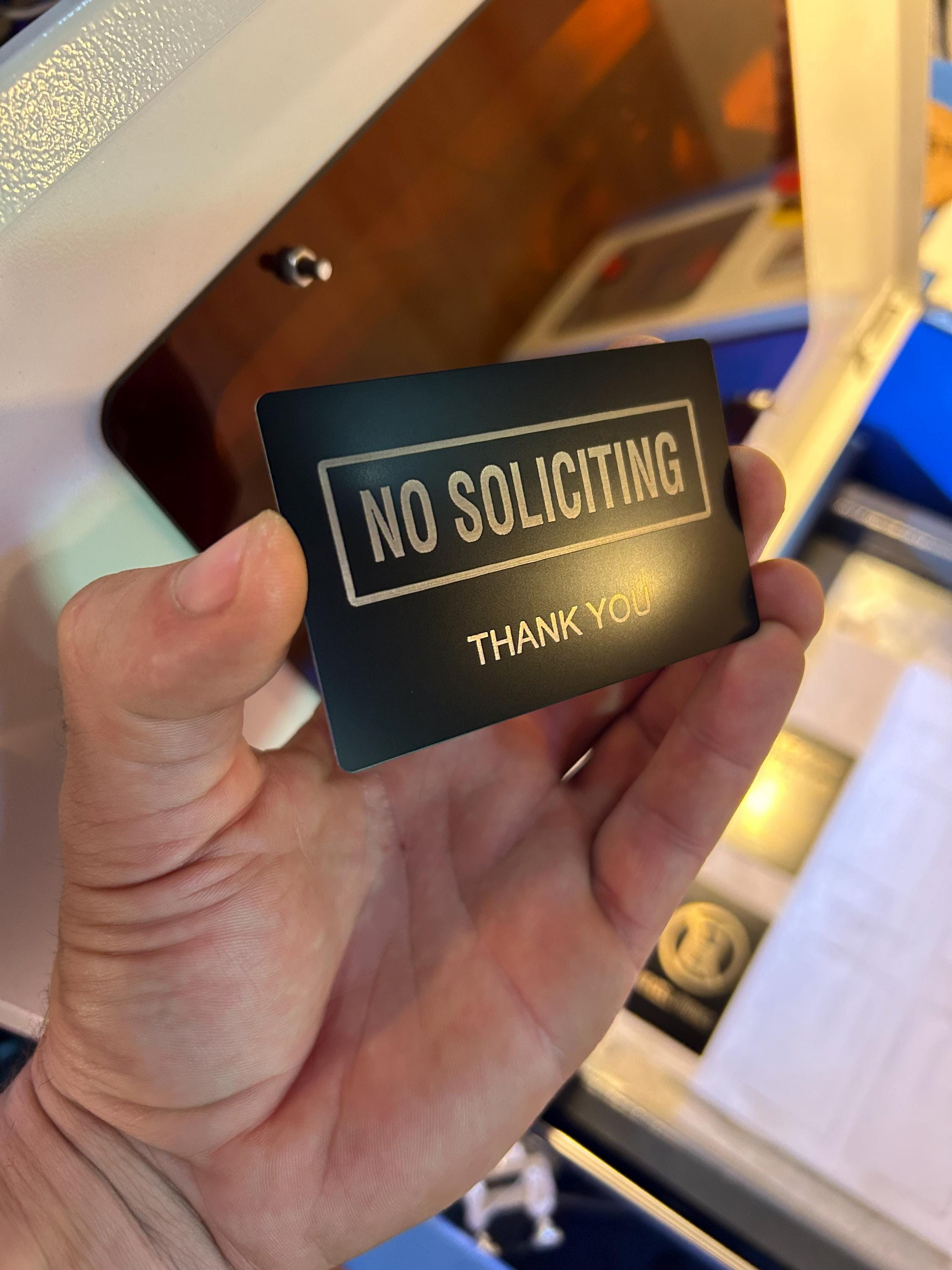 Side angle of anodized aluminum laser engraved black/silver novelty placard with “No Soliciting” and Thank You beneath