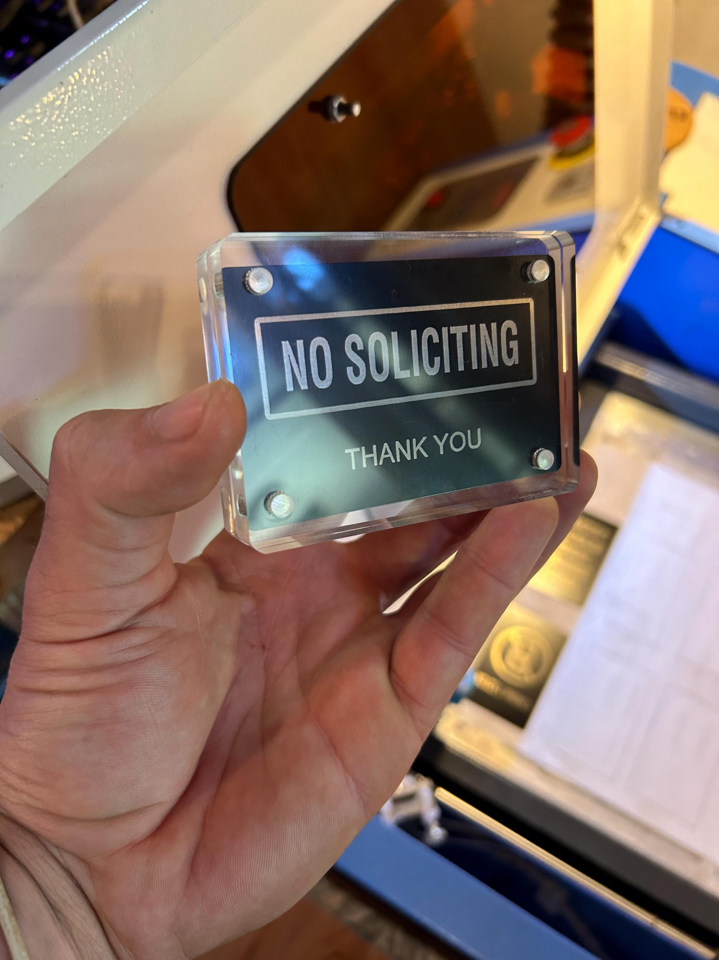 Hand holding a laser engraved black/silver metal 'No Soliciting' retail/residential signage card