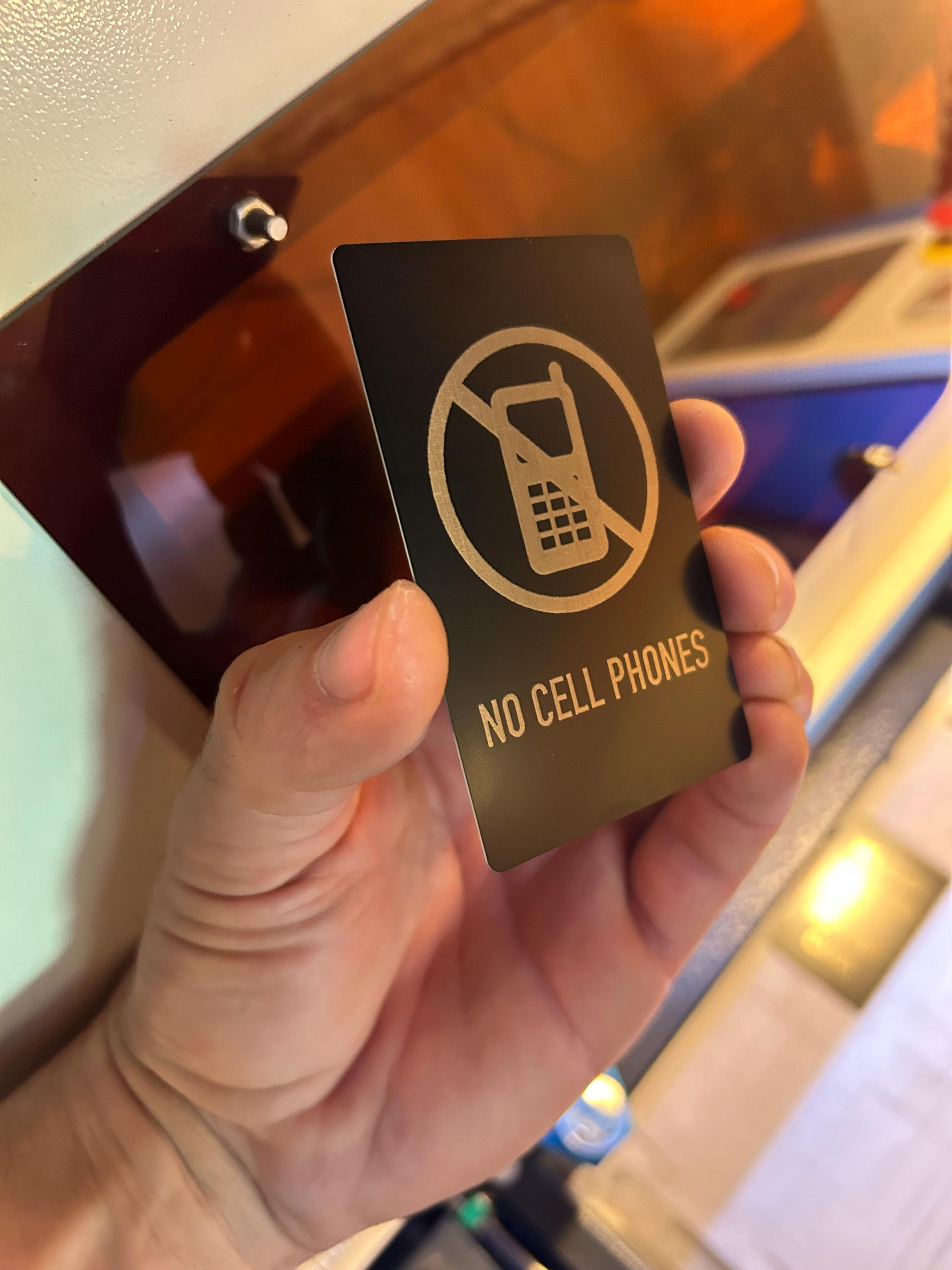 Hand holding a 'No Cell Phones' placard in front of a blurred background