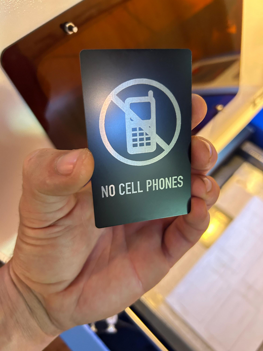 Hand holding a metal 'No Cell Phones' sign in front of a screen