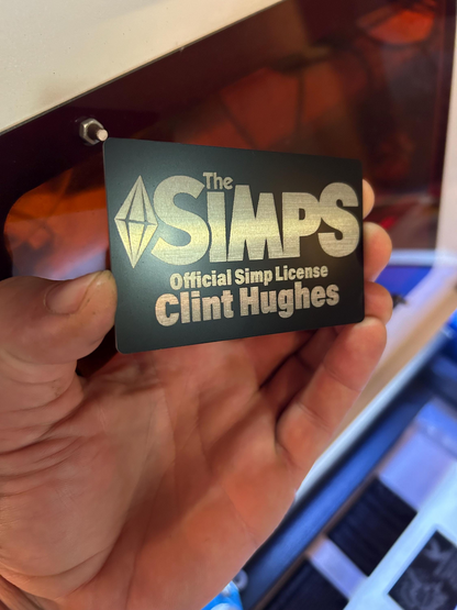 Hand holding a 'The Simps' license gag gift card with custom name engraving