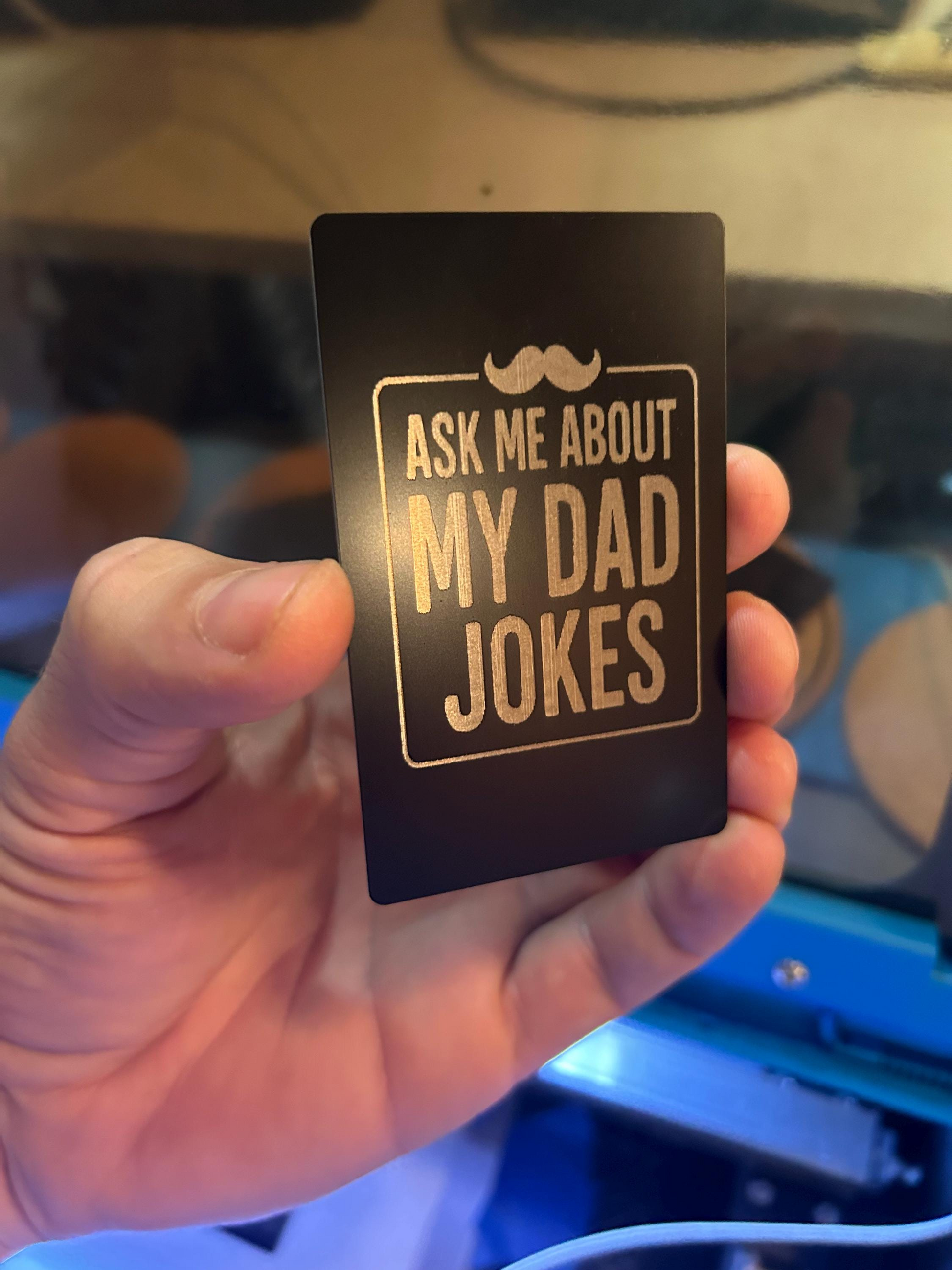 Person holding a funny engraved keepsake card in black and silver anodized aluminum with dad joke design