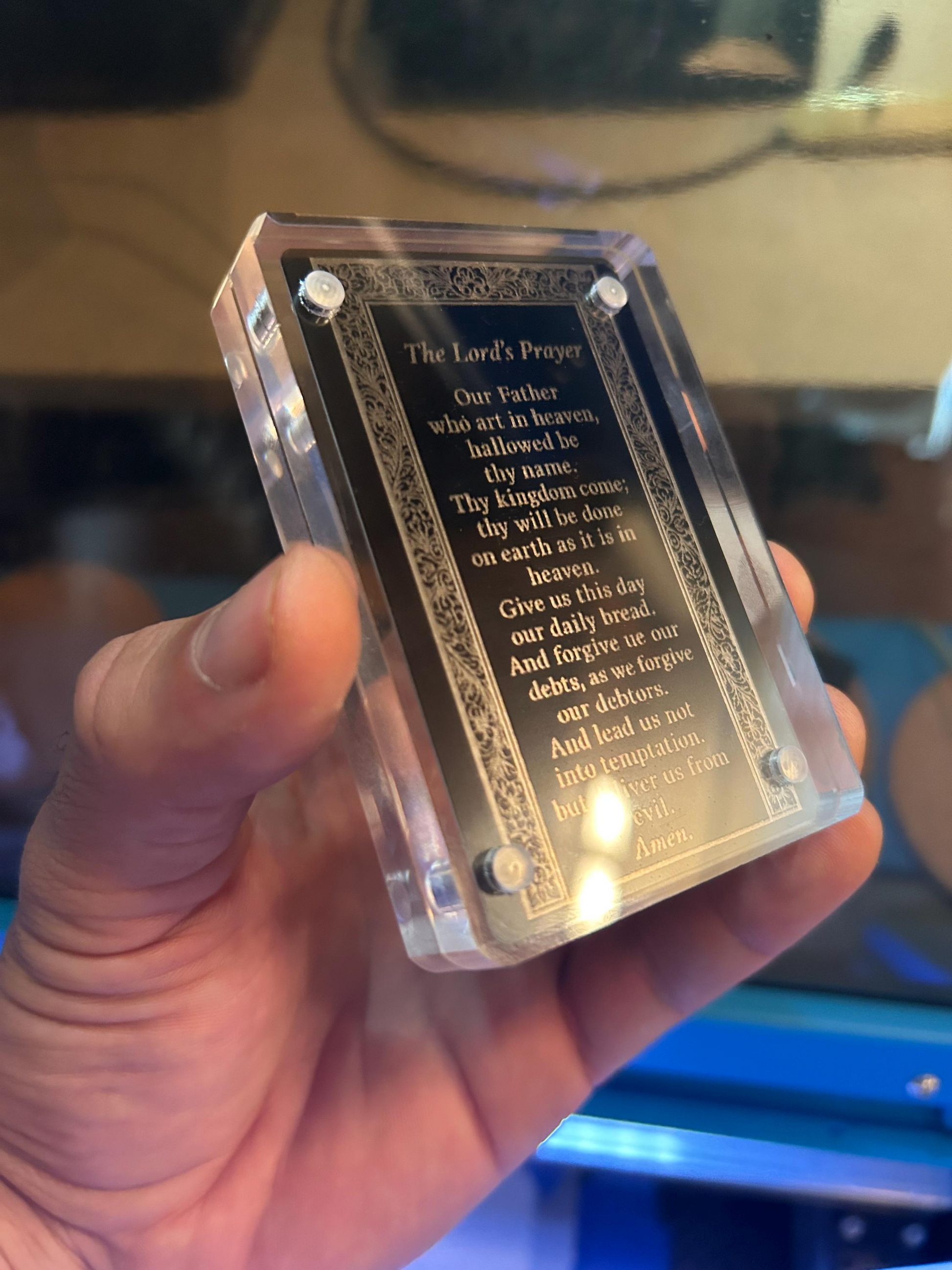 Hand presenting a laser cut religious flash card engraved with The Lord’s Prayer in black/silver anodized finish
