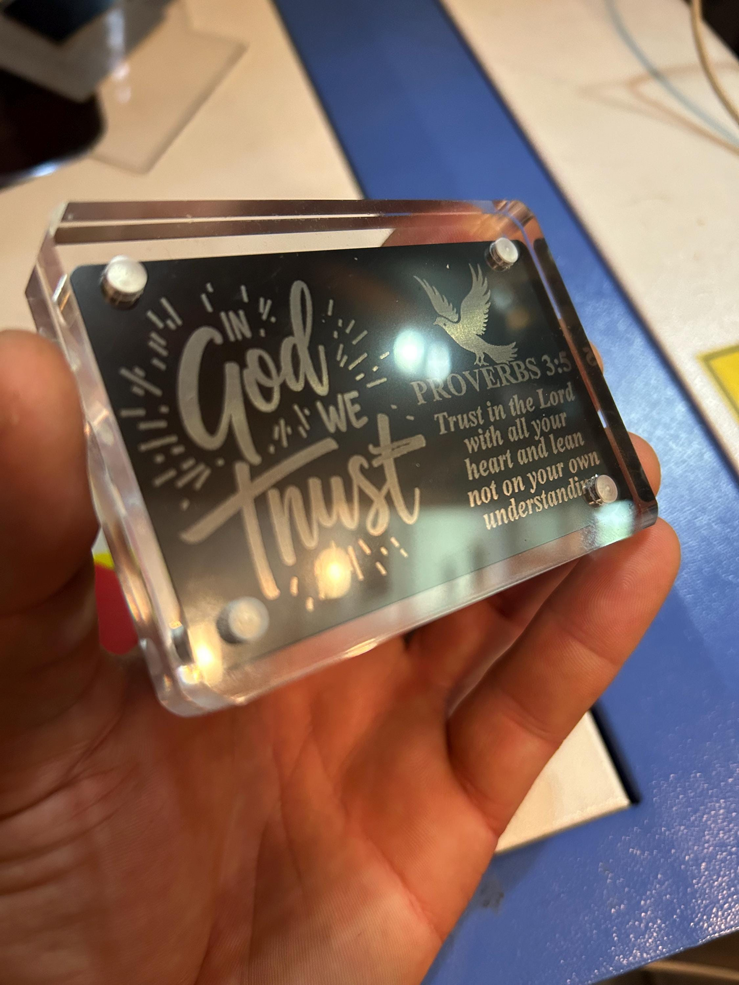 Hand holding a clear acrylic display case with demonstration of metal engraving with text and design.