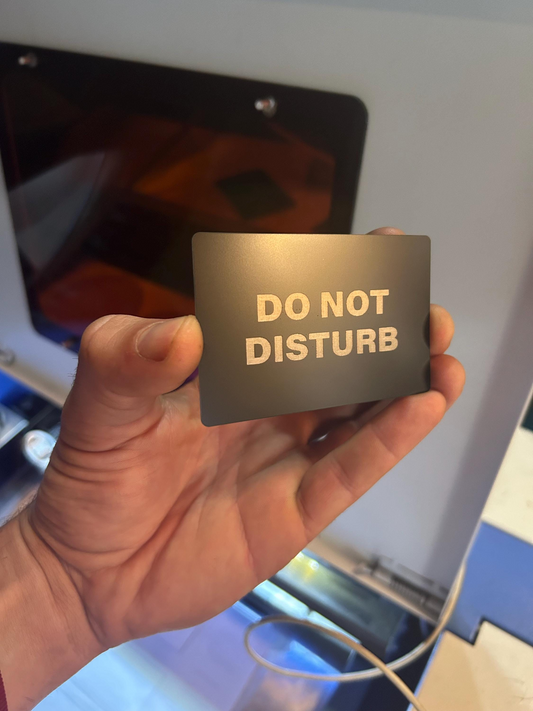 Hand holding a black and silver laser engraved metal placard with “Do Not Disturb” text