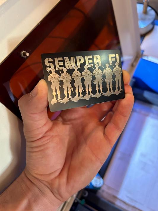 Hand holding a metal placard with military-themed design and 'SEMPER FI' text.