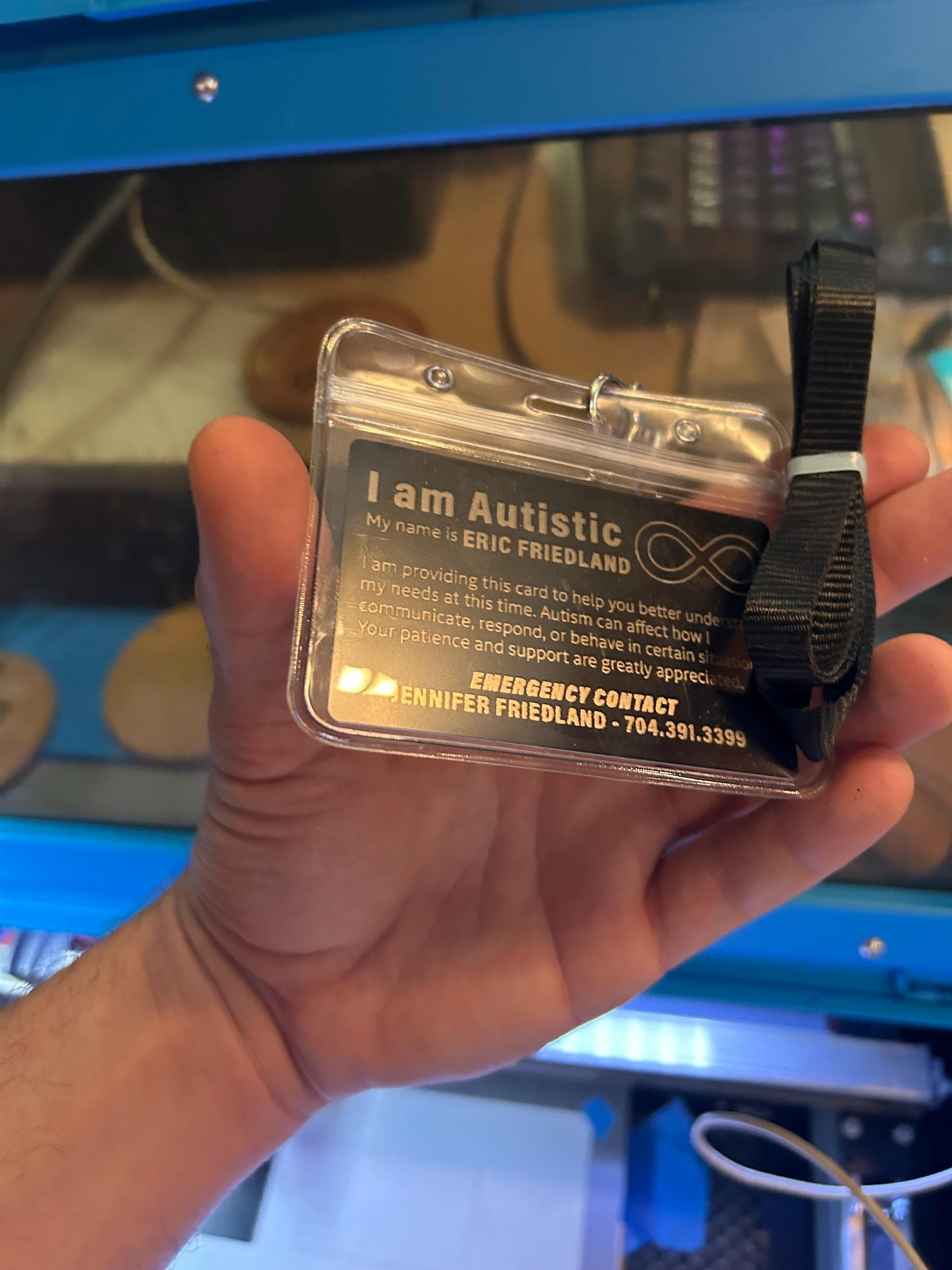 Hand holding a 'I am Autistic' identity card with text and contact information in badge holder and lanyard