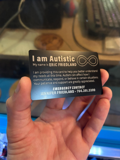 Hand holding a black/silver metal autism awareness id card with customized text