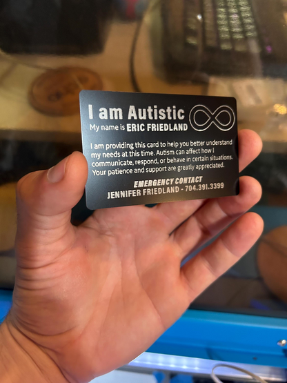 Hand holding a black anodized aluminum metal medical id badge card with text about autism and contact information.