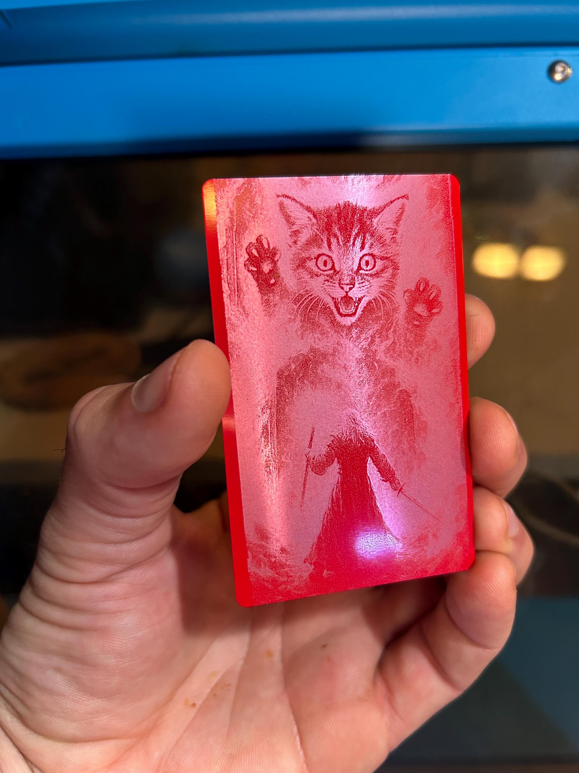 Red metal gift card with a giant magical cat illustration held by a hand against a blurred background