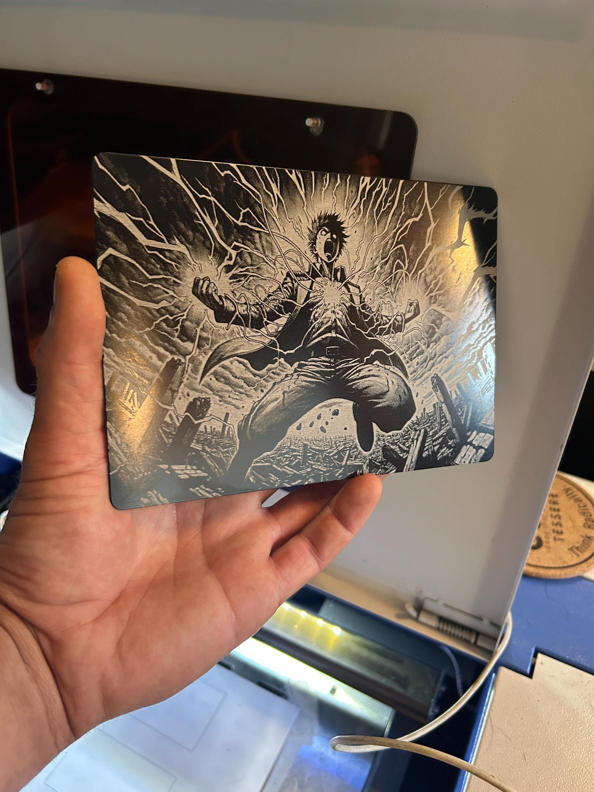 Hand holding a matte black anodized aluminum 5x7 placard with laser engraved line art