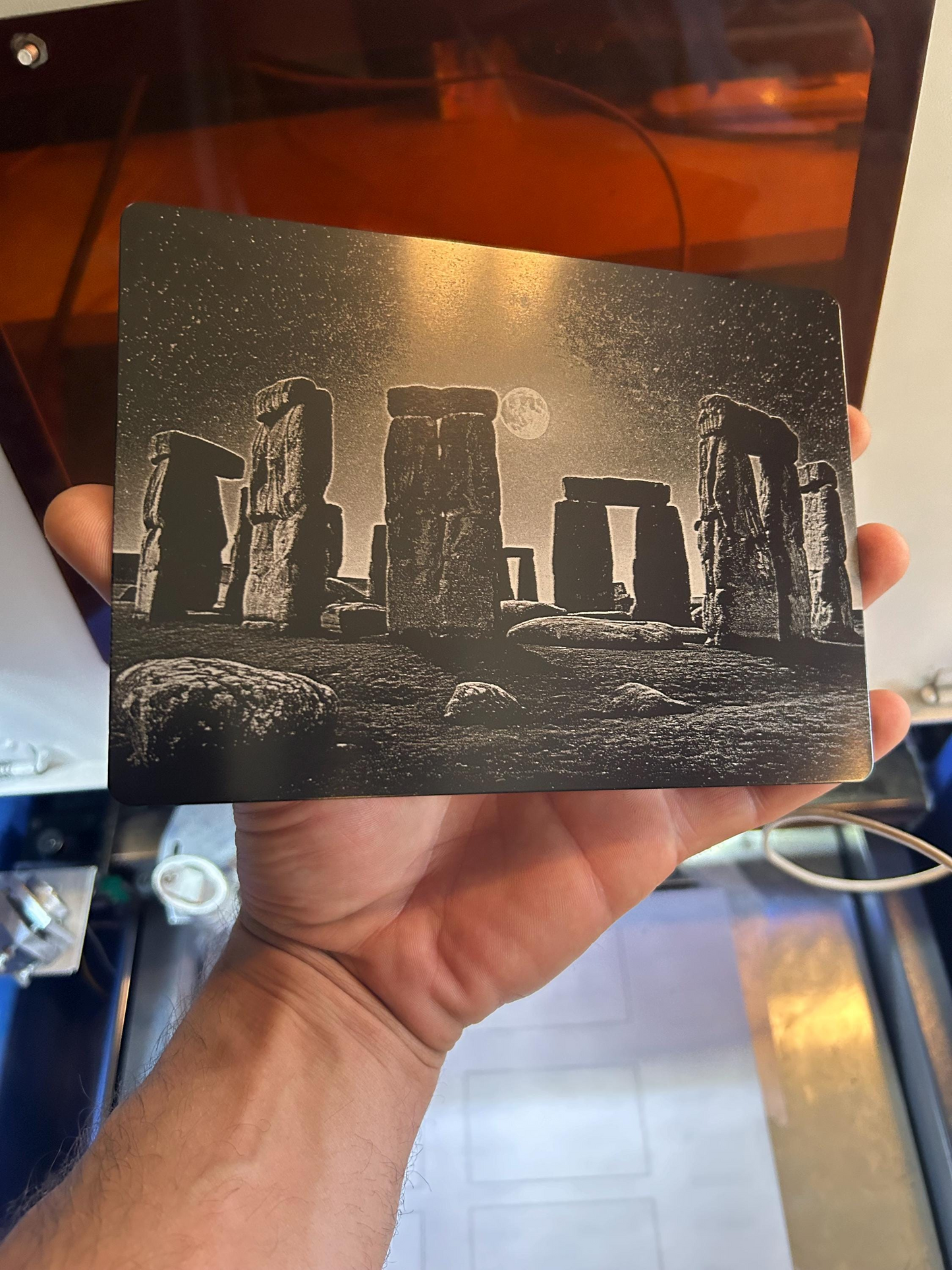 Hand holding a laser engraved world wonder in size 7x5" in matte black/silver metal stone henge illustration