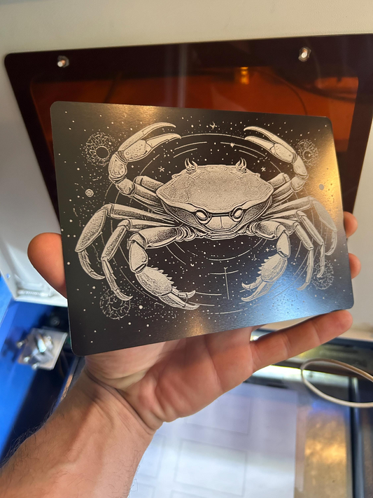 Hand holding a decorative zodiac art with a detailed illustration of a crab against a metallic background.