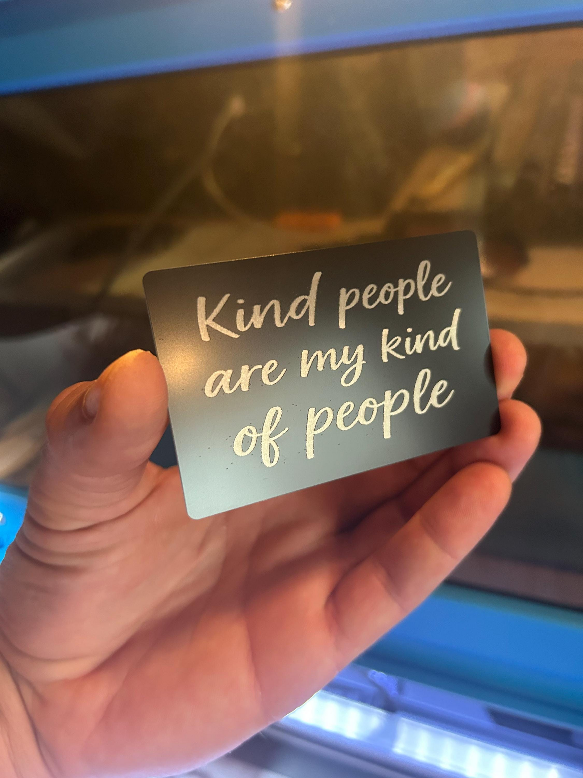 Hand holding a metal wallet insert giftcard with 'Kind people are my kind of people' text.