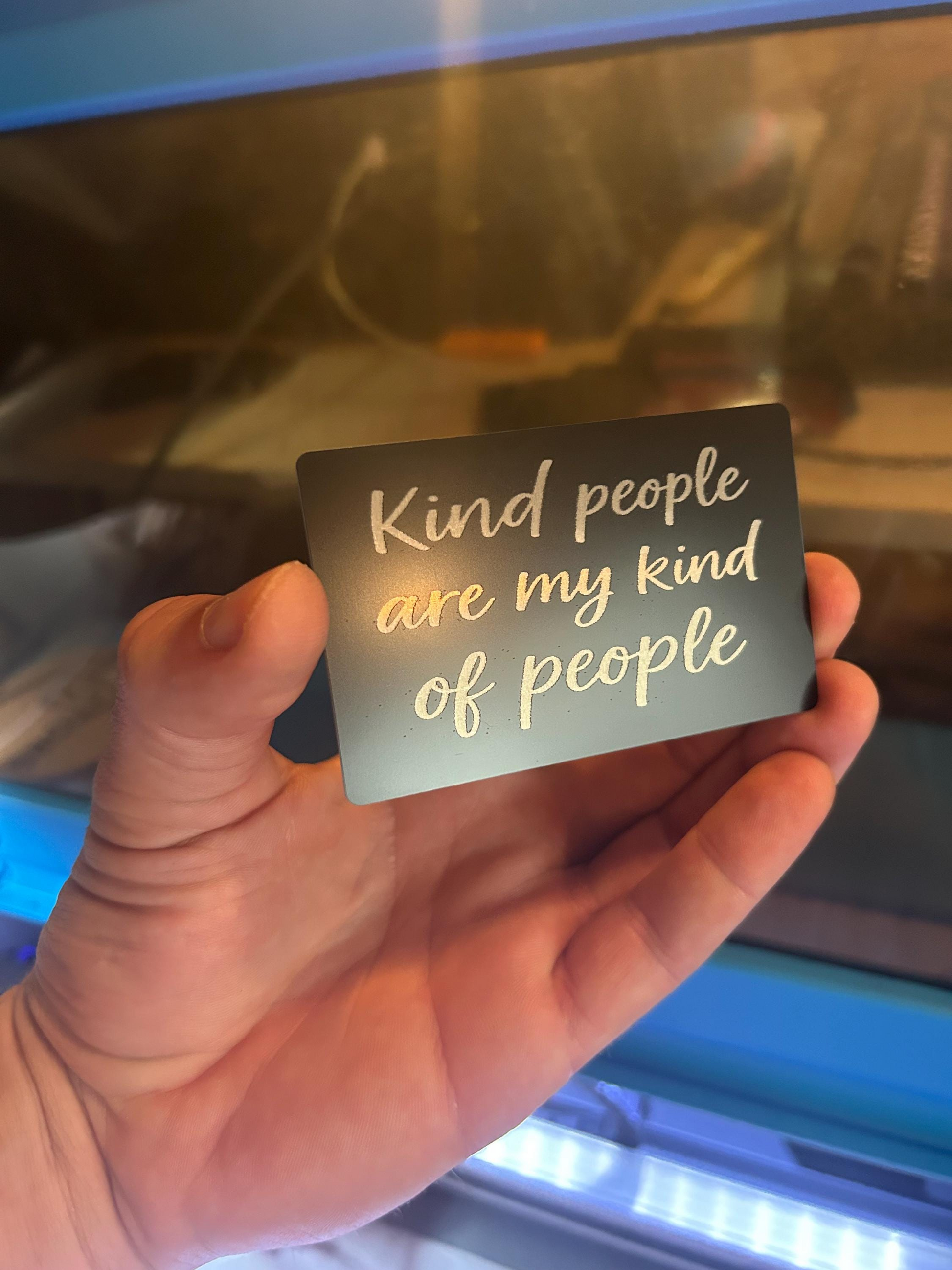 Hand holding a laser engraved anodized aluminum keepsake card with 'Kind people are my kind of people' text.