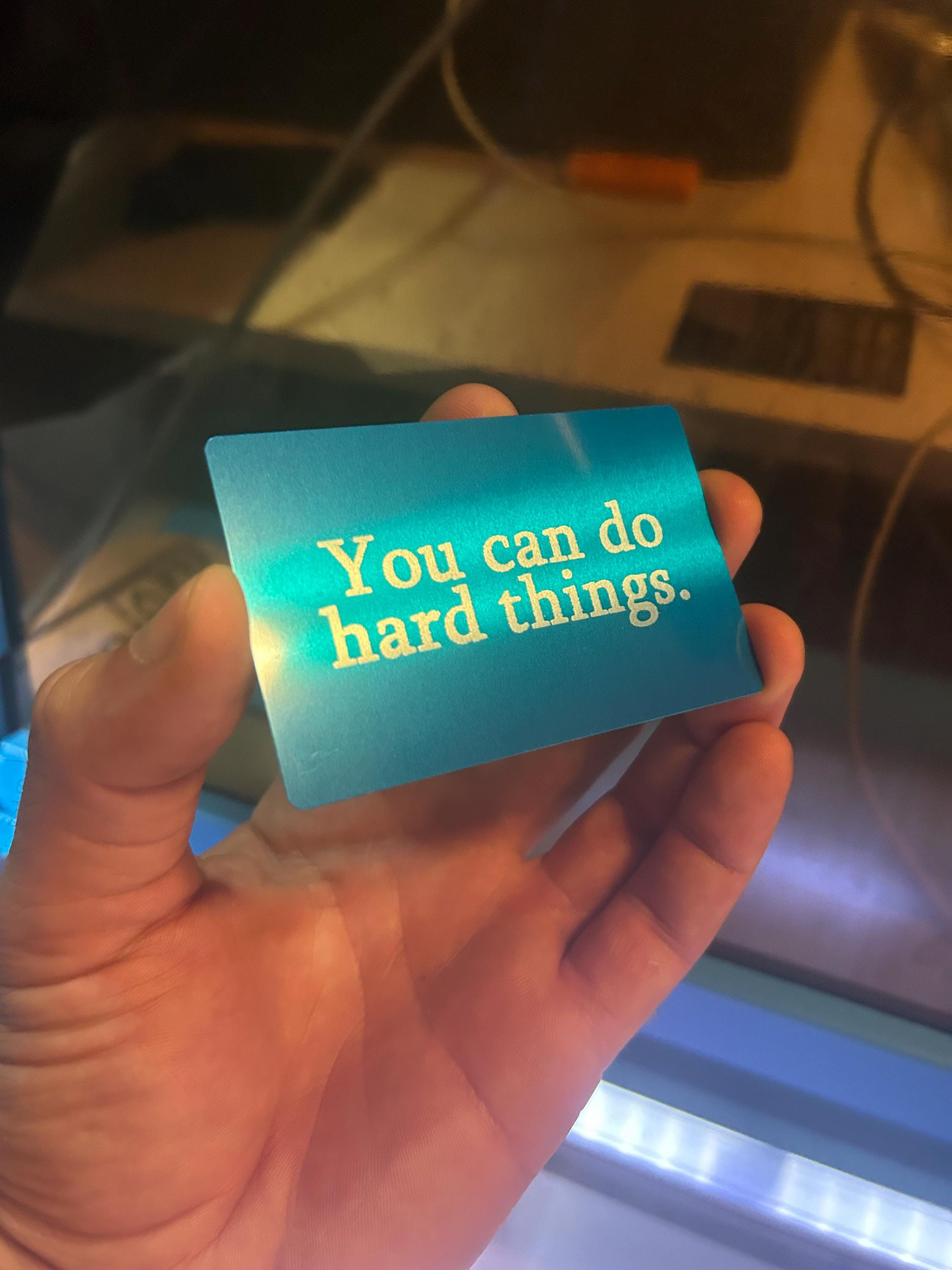 Hand holding a blue silver/blue metal keepsake card with 'You can do hard things' text  in anodized aluminum.