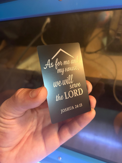 Hand holding a metal business card with laser engraved text 'As for me and my house, we will serve the LORD' from Joshua 24:15. 