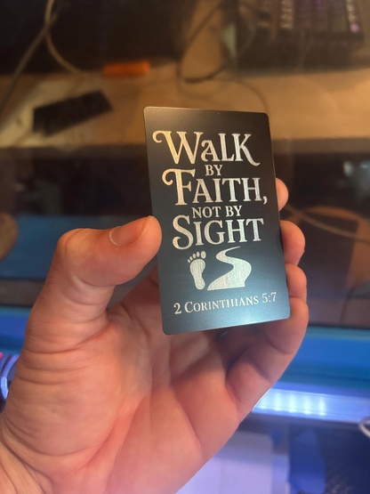 Hand holding a metal card with 'Walk by Faith, Not by Sight' typography and 2 Corinthians 5:7 reference.