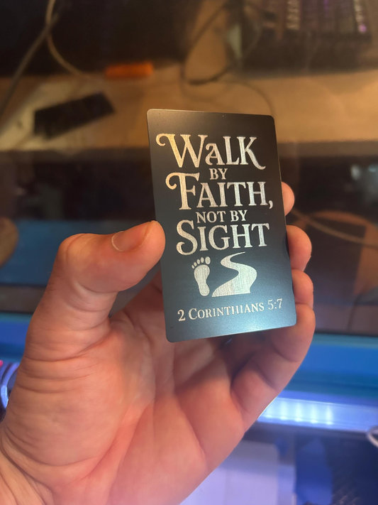 Hand holding a metal card with 'Walk by Faith, Not by Sight' typography and 2 Corinthians 5:7 reference.
