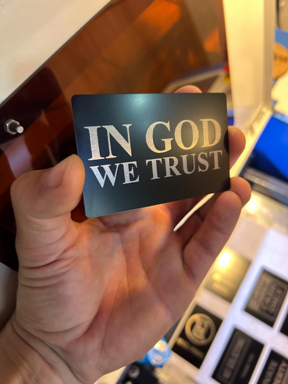 Hand holding a laser engraved placard with 'IN GOD WE TRUST' text laser engraved