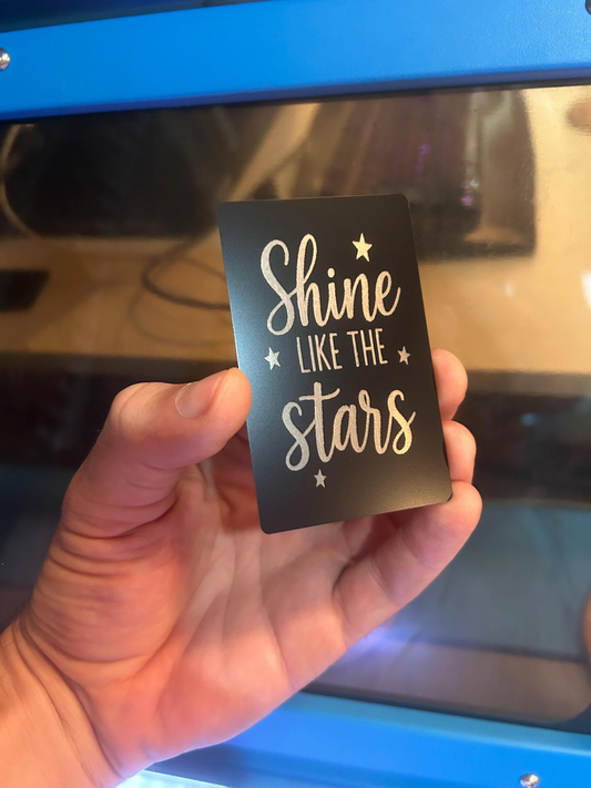 Hand holding a laser engraved keepsake with inspirational text in front of a blurred cnc machine background