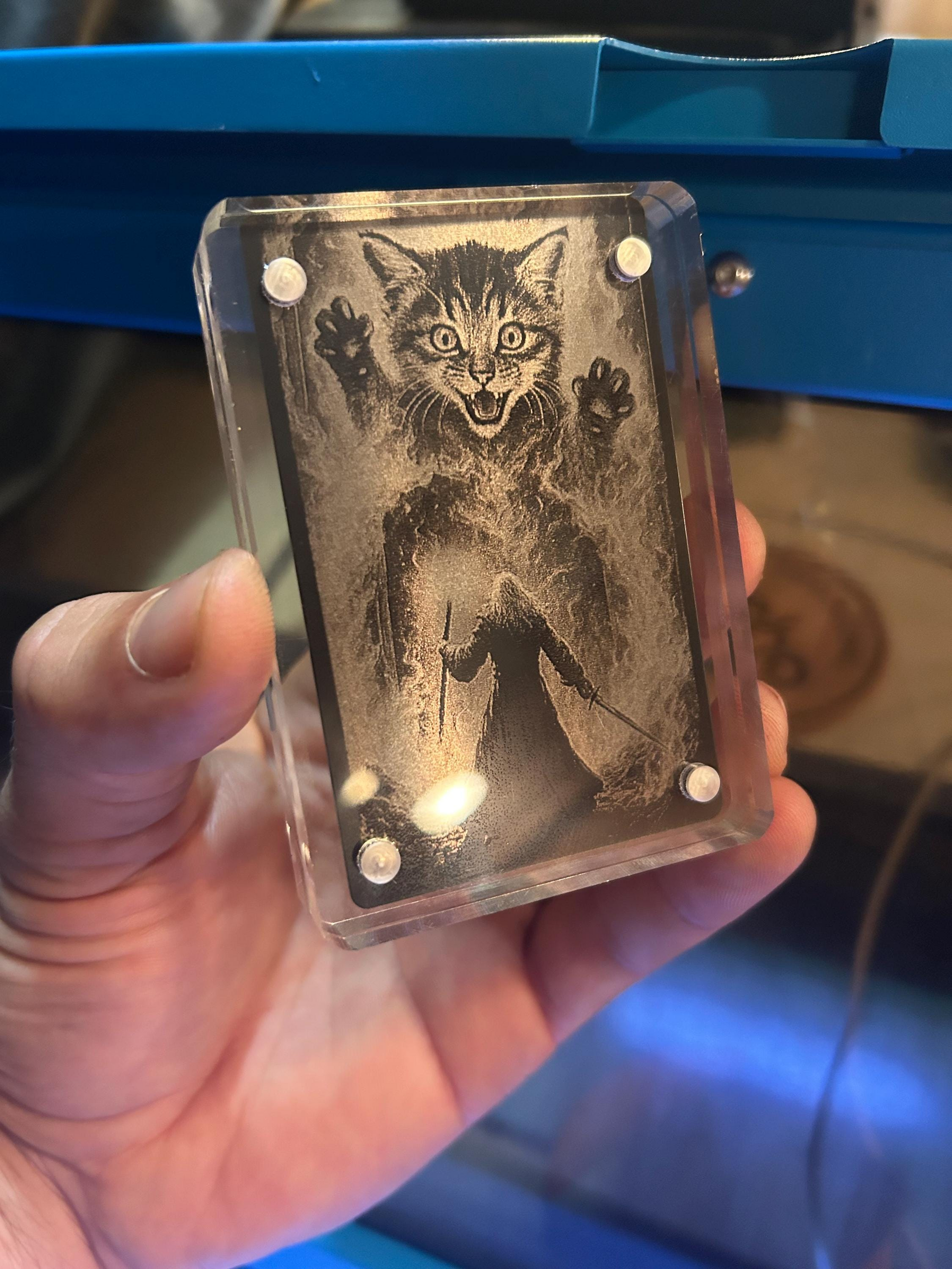 Hand holding a transparent block with a carved image of a cat and a person in a dark outfit.