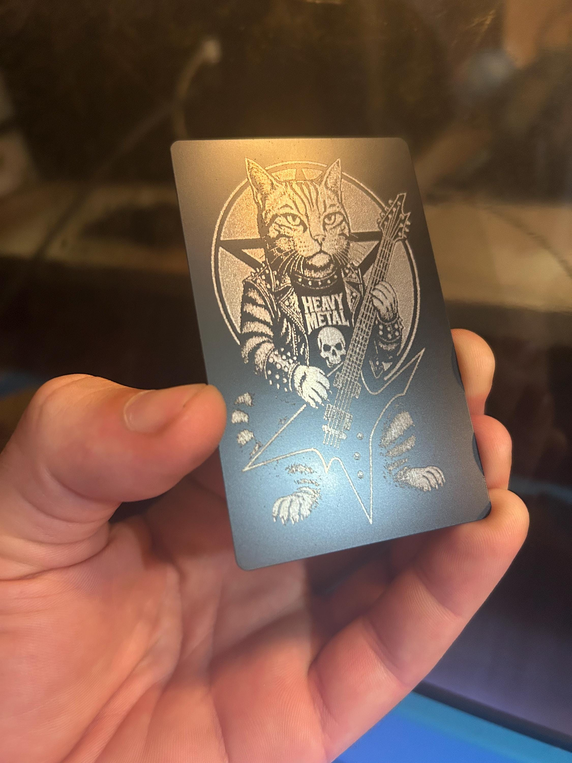 Hand holding a laser engraved novelty keepsake card with a punk rock cat playing guitar design in black/silver