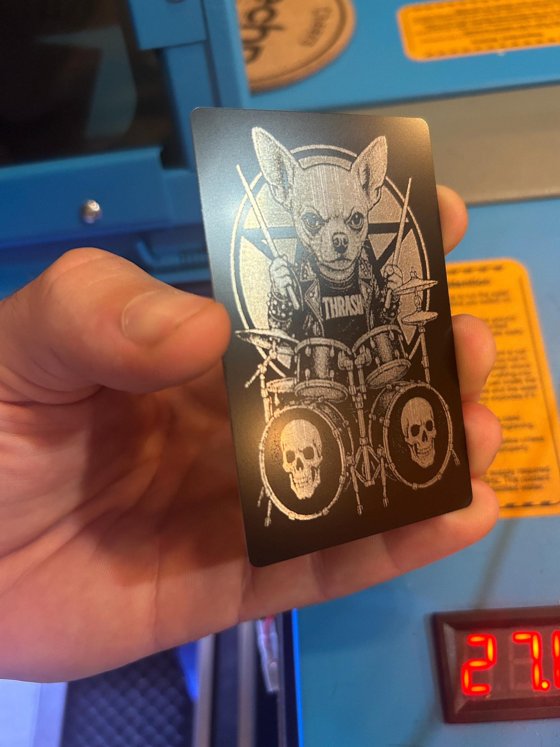 Hand holding a card with a heavy metal dog illustration and 'Thrash' band logo against a blue background.