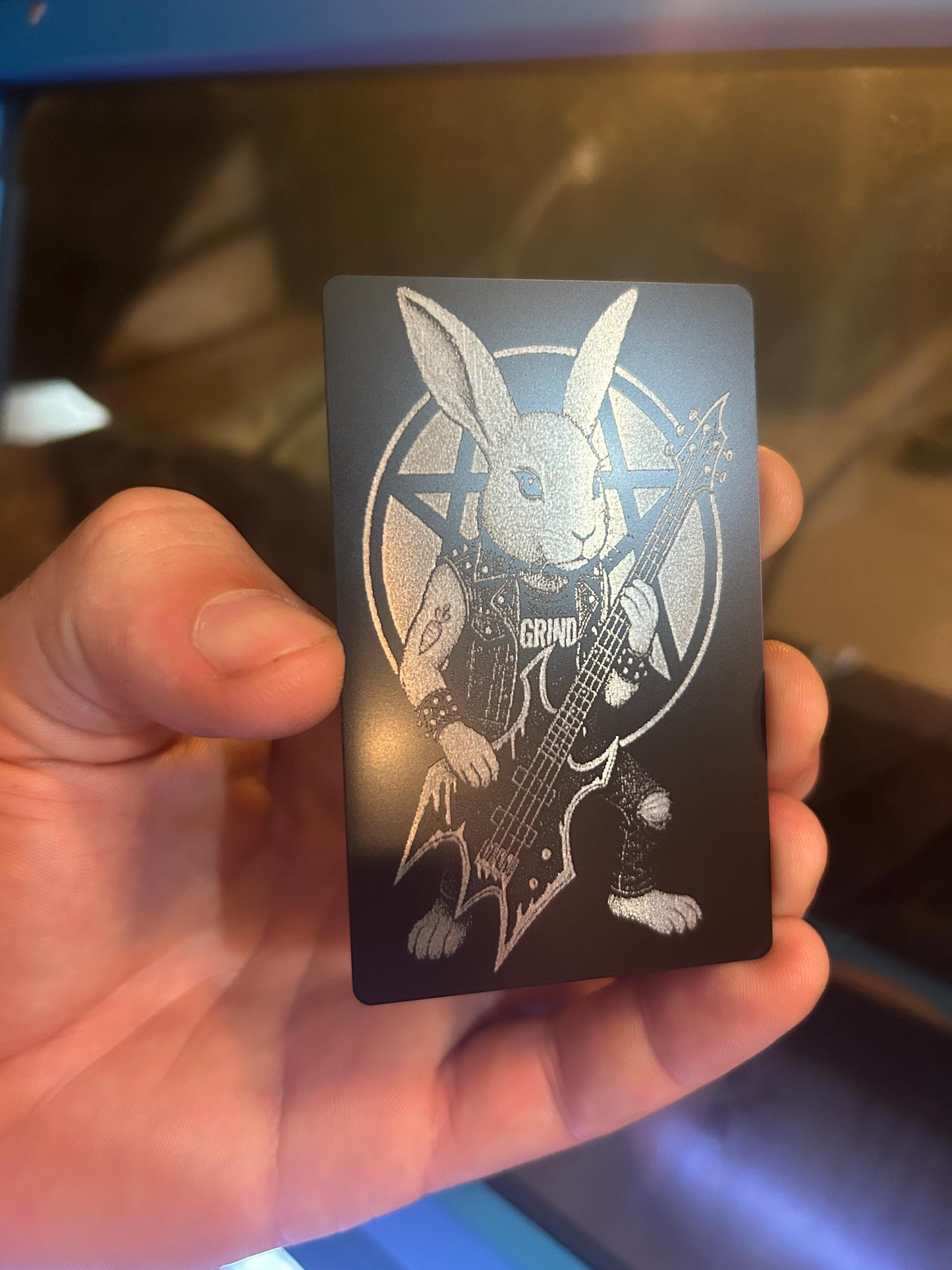 Hand holding a black anodized aluminum keepsake card with a bassist bunny illustration design