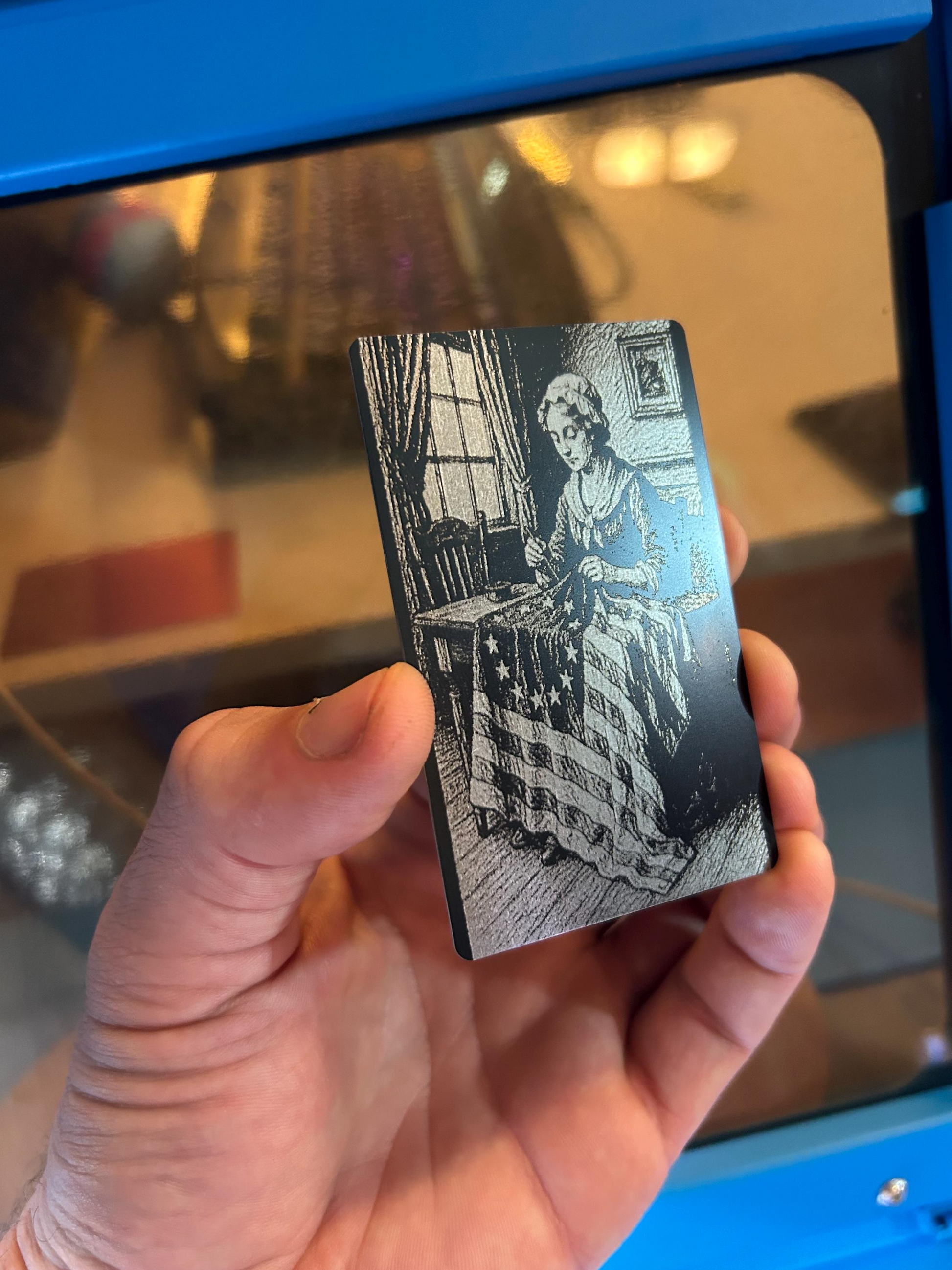 Hand holding a small card with an engraved patriotic image of american flag and betsy ross sewing