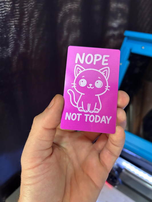 Hand holding a pink card with a cat illustration and text 'NOPE NOT TODAY' against a blurred background.