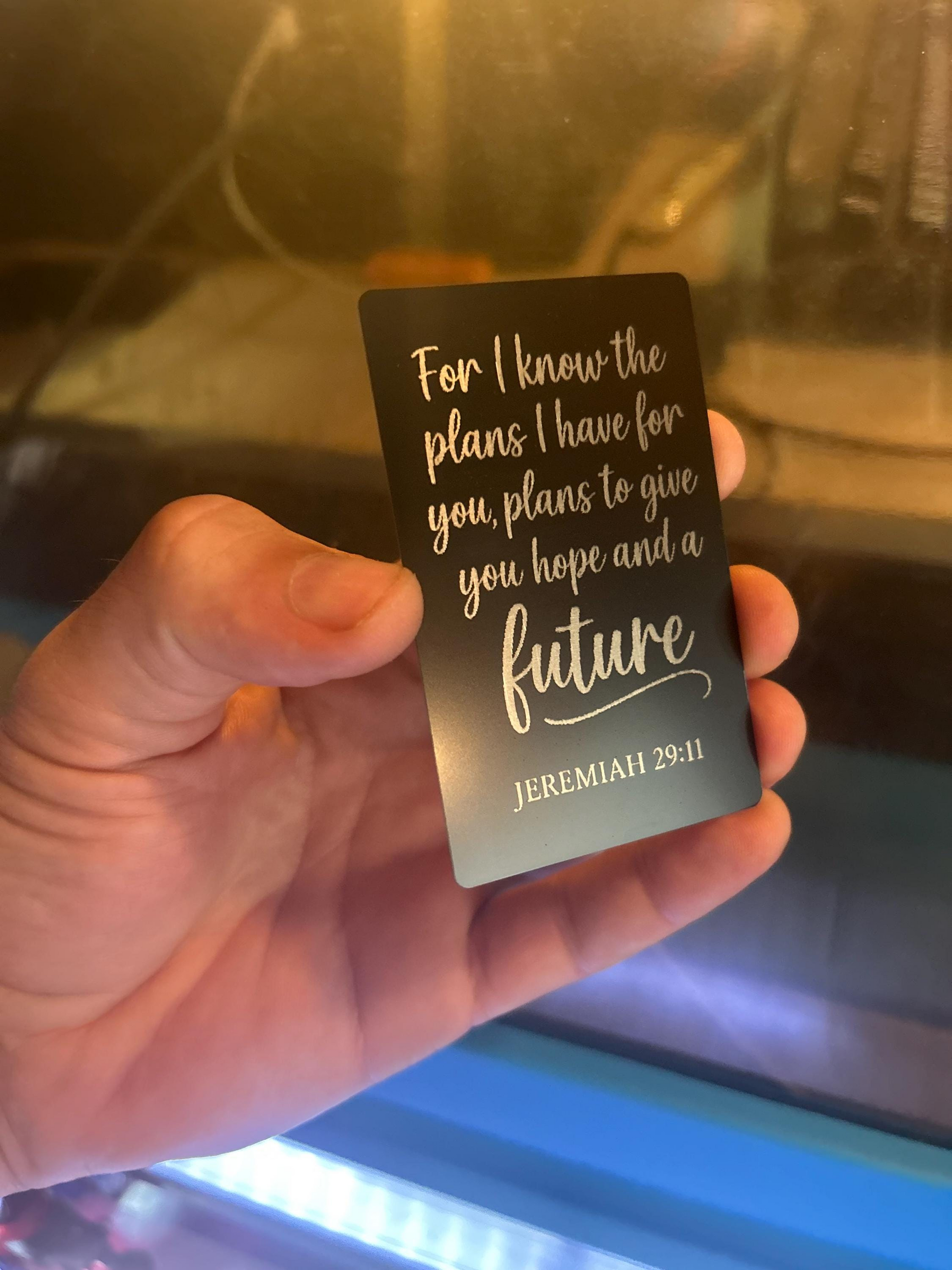 Person holding a faith inspired engraved metal keepsake card – “For I Know the Plans I Have For You” design with blurred backdrop