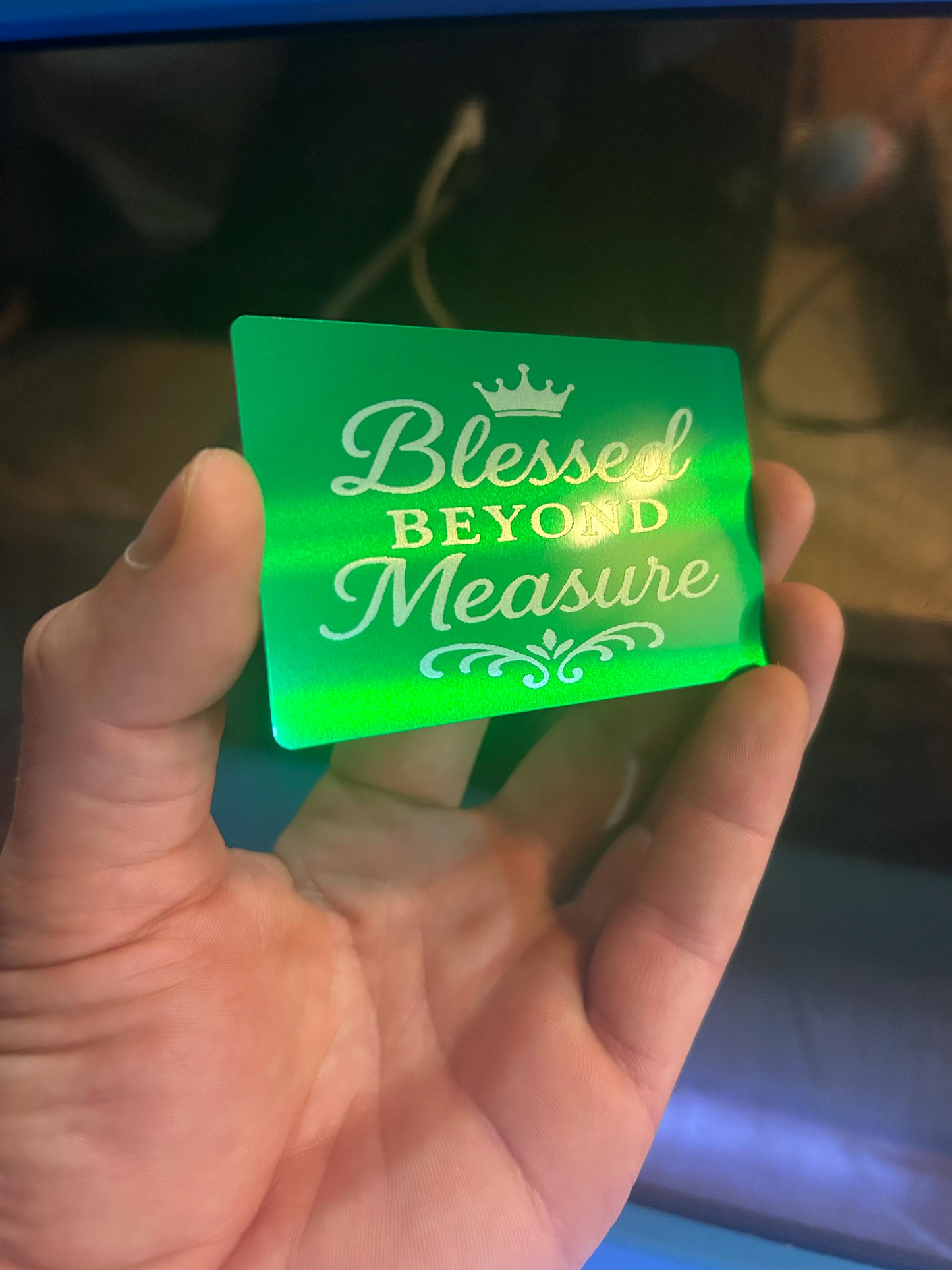 Hand holding a green and silver metal gift card with 'Blessed Beyond Measure' and crown logo