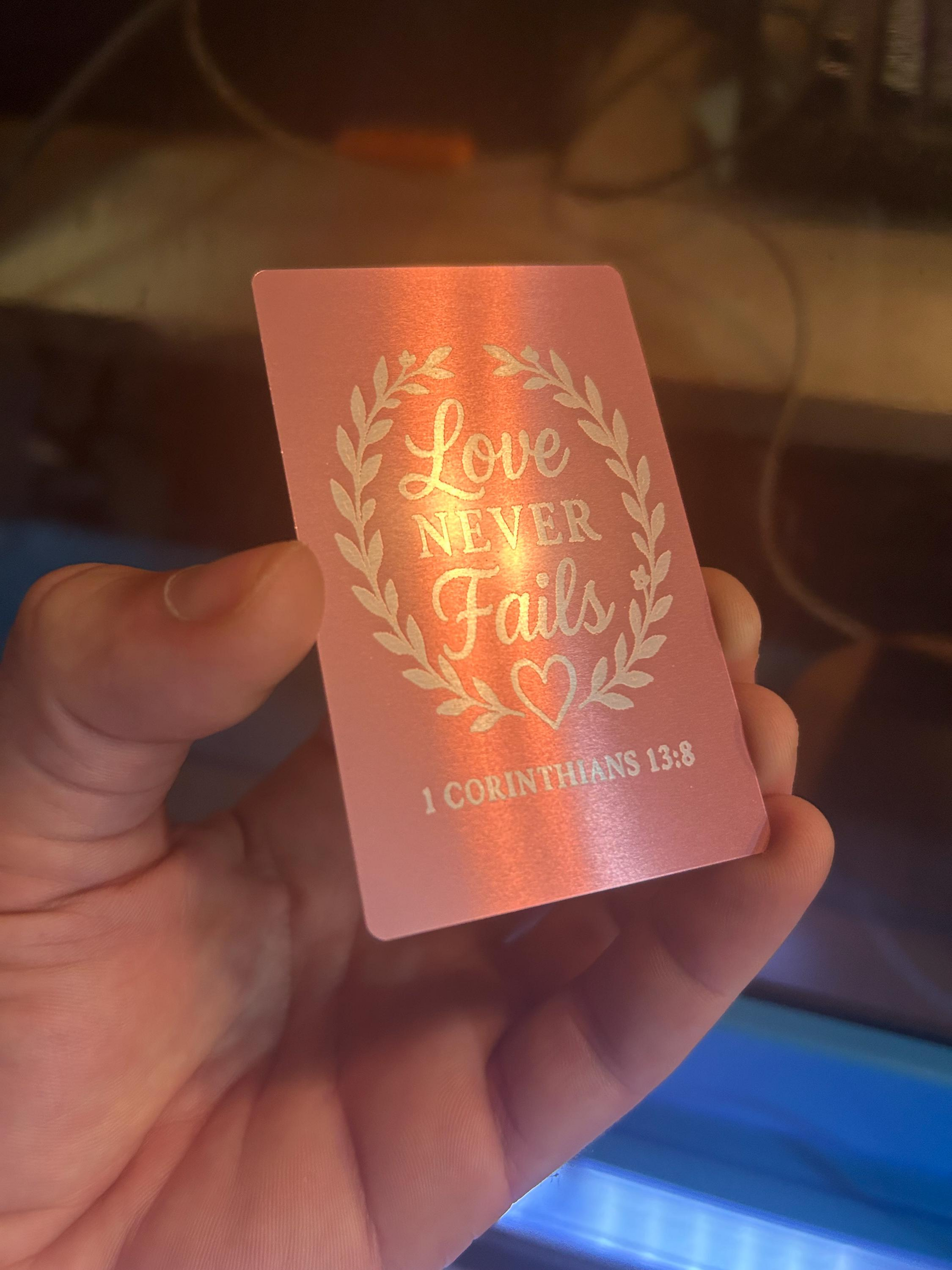 Hand showcasing a custom rose gold engraved keepsake card with Christian verse “Love Never Fails” typography design