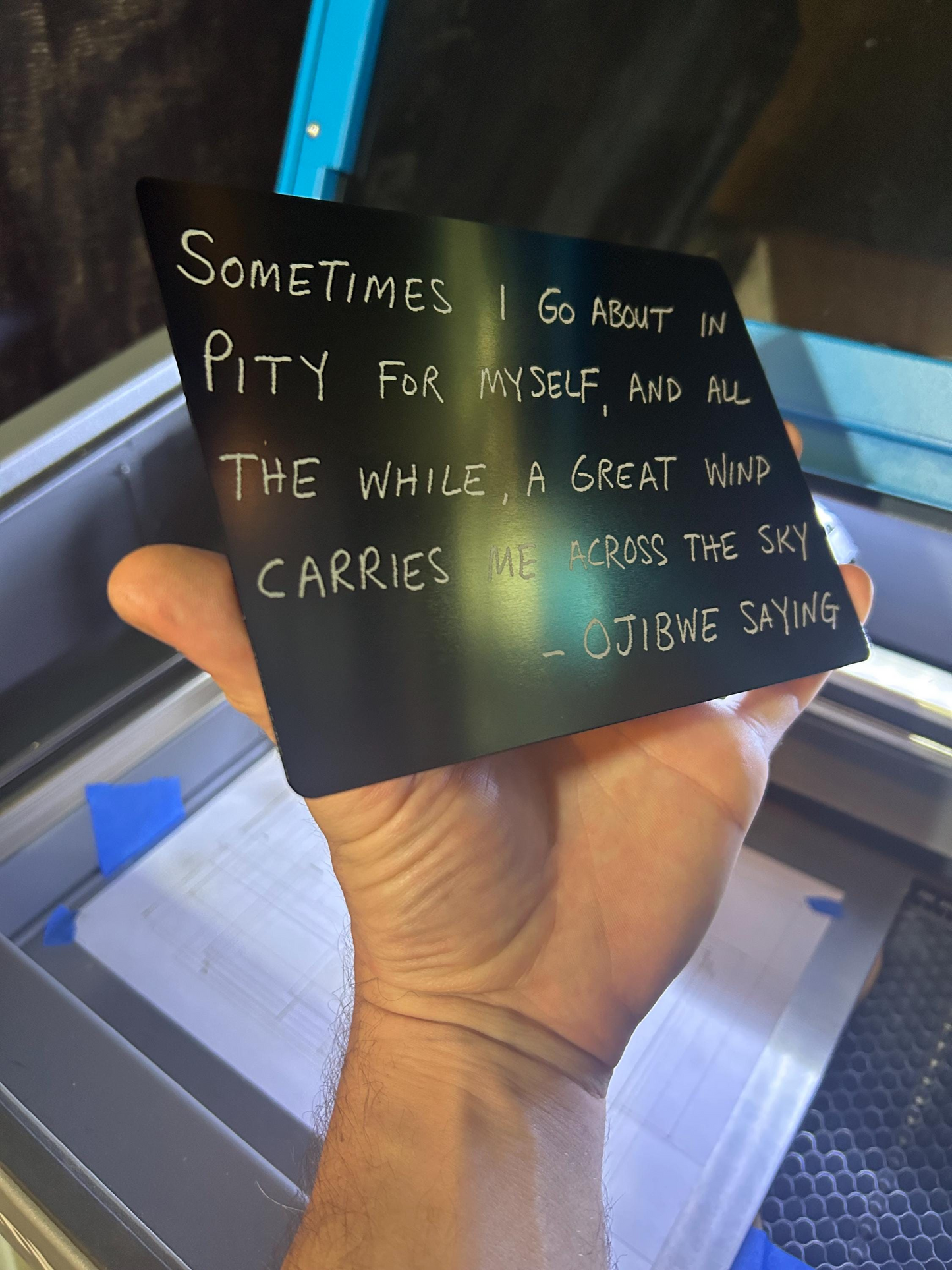 Hand holding a metal decorative plaque with inspirational thoughtful text against a blurred indoor background