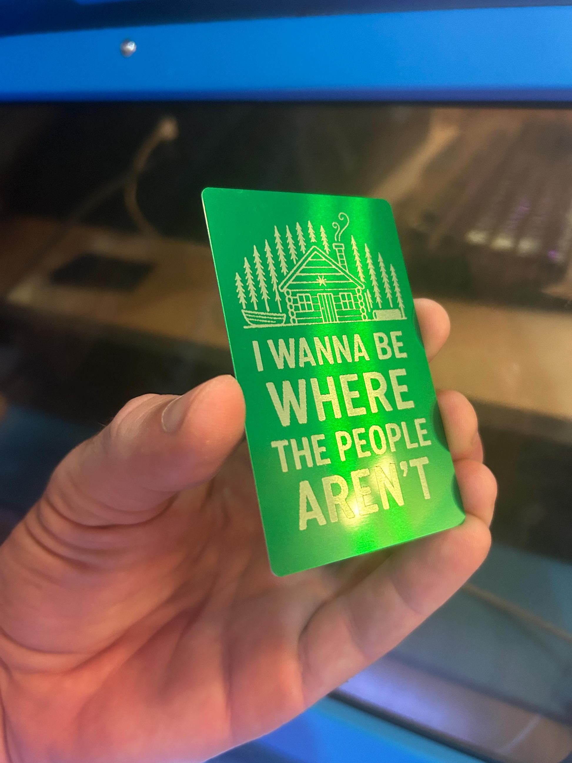 Hand holding a laser engraved metal keepsake card that reads "I Wanna Be Where The People Arent"